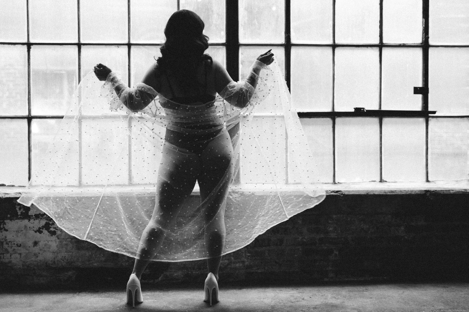 A black and white photo showing silhouettes of a woman in a sheer robe with graceful movements against a bright window.