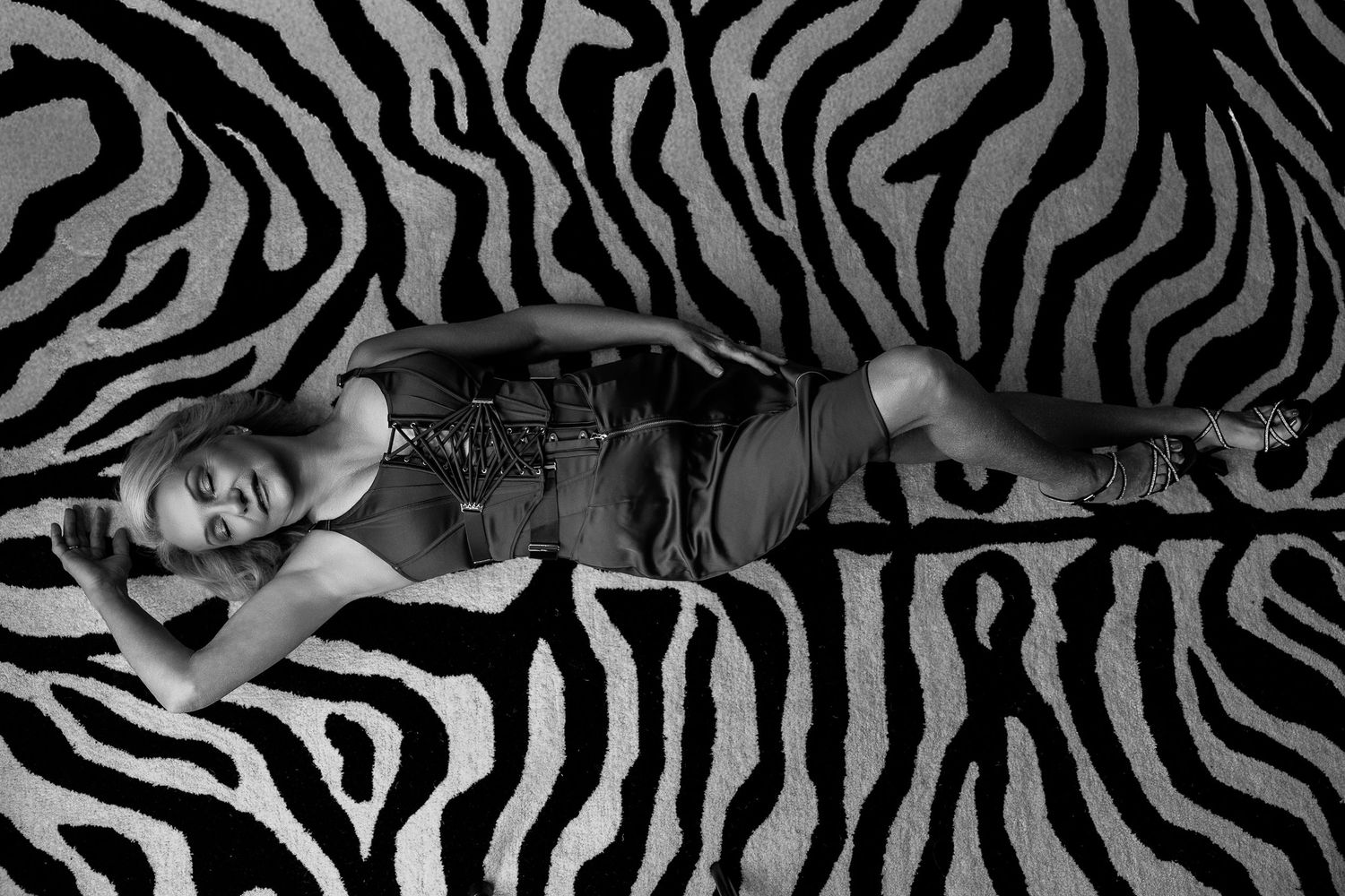 Woman in dark outfit lying on bold black and white zebra print fabric in a striking monochrome photo.