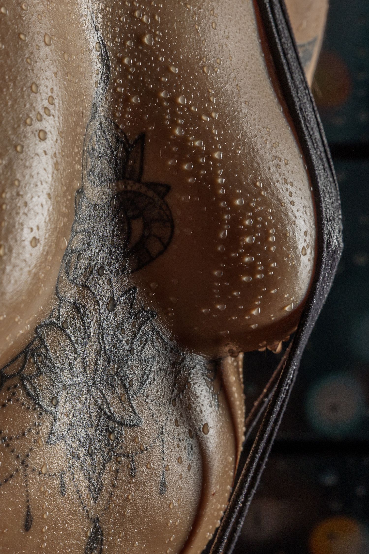 Close-up of wet tattooed skin with water droplets and floral ink designs, with a dark strap visible.