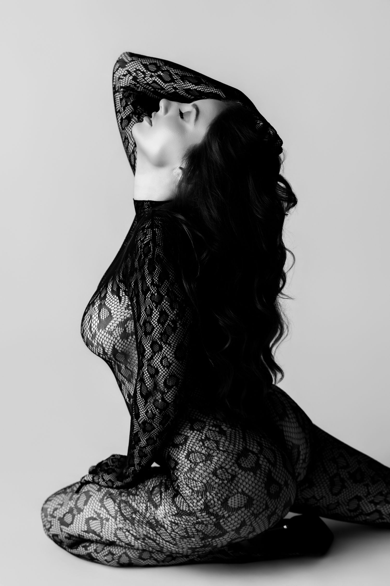 Black and white photo of a woman in lace bodysuit sitting gracefully on floor with long dark hair flowing.
