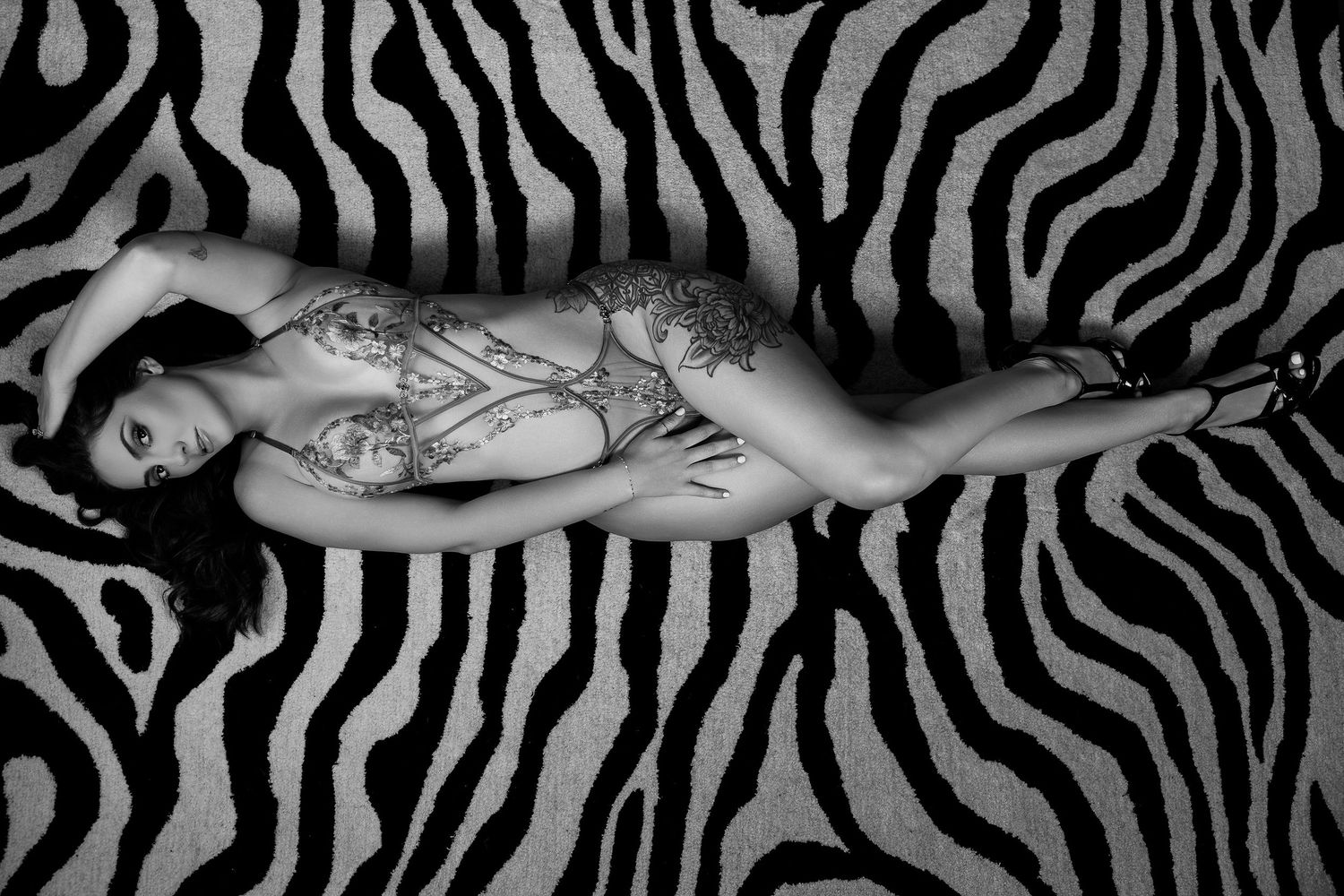 Woman with tattoos posing on a zebra print rug in a black and white artistic boudoir photograph.