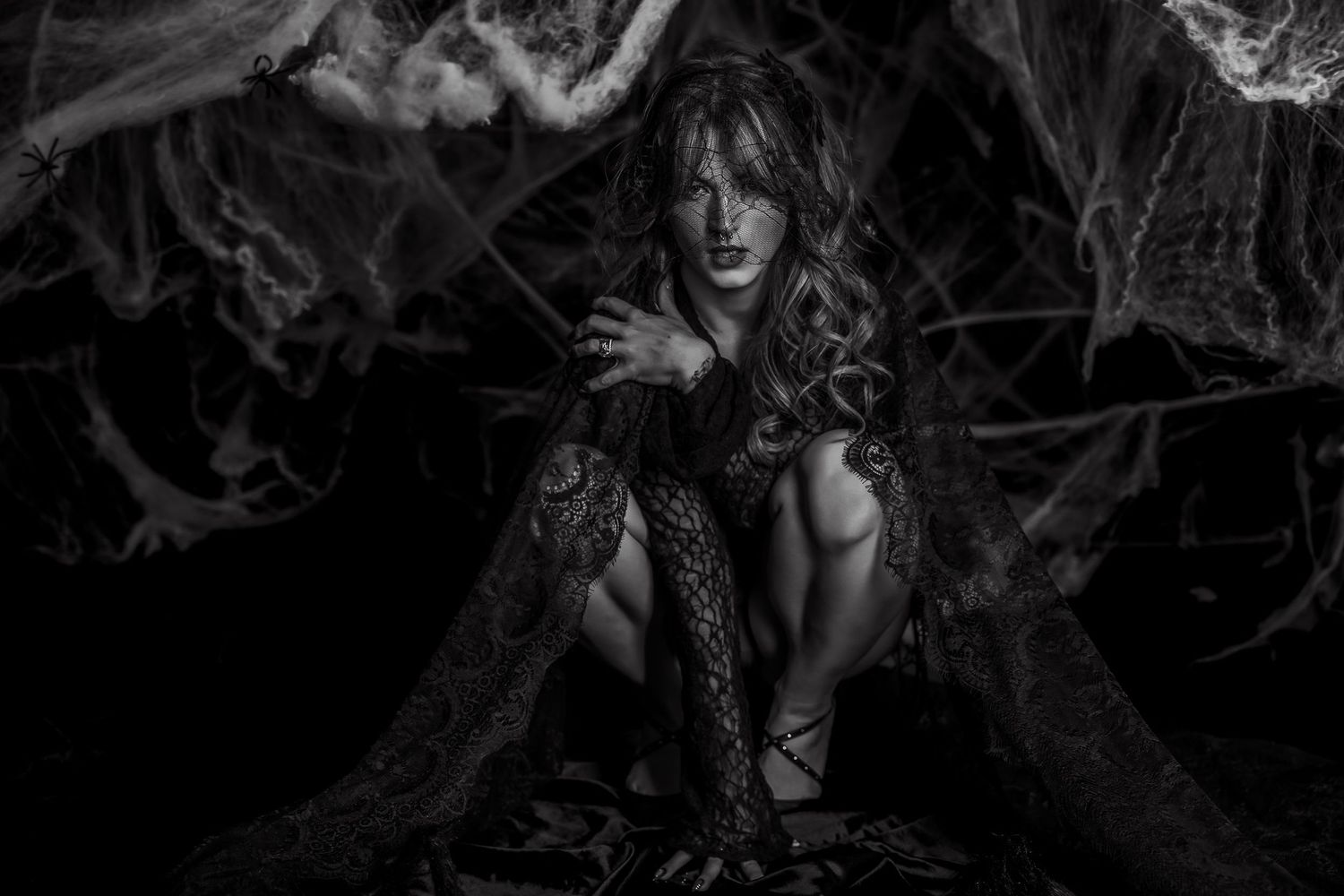 Black and white photo of a woman in dark lace surrounded by spider webs in a dramatic gothic fantasy setting.