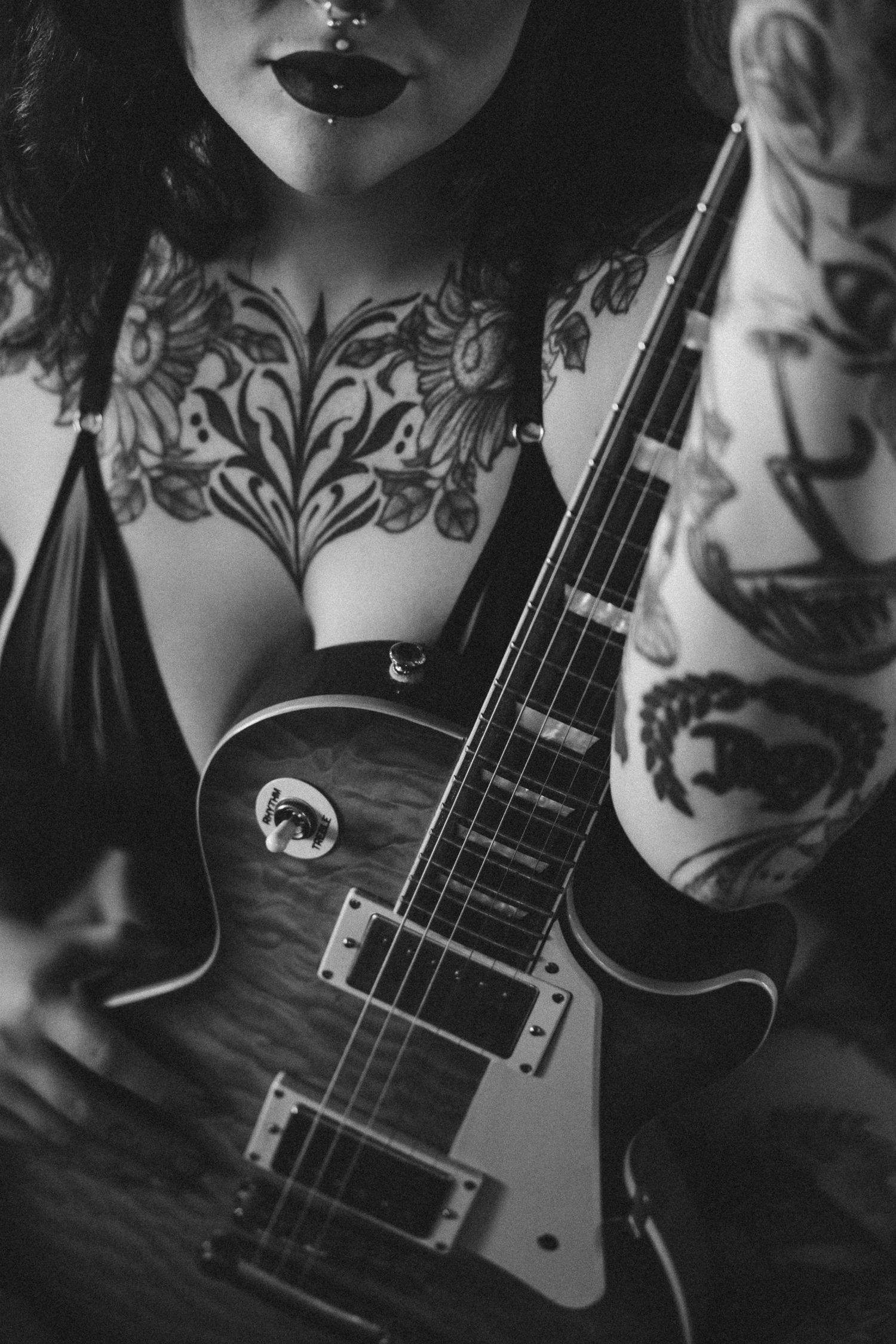 Black and white photo of tattooed woman holding a Les Paul electric guitar, showcasing intricate body art.