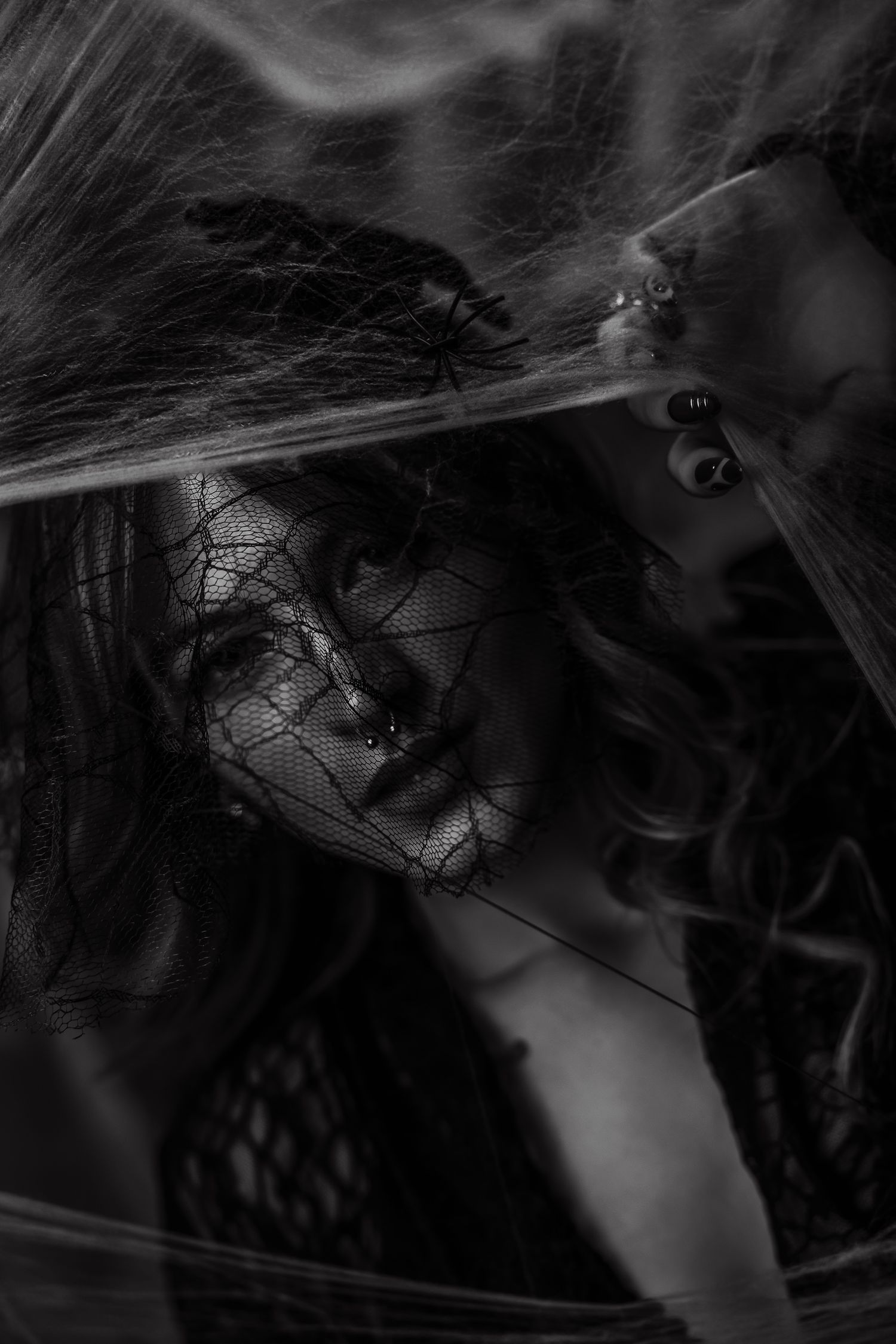 Black and white portrait of a woman with spider web veil and spiders, dark gothic Halloween aesthetic photography.