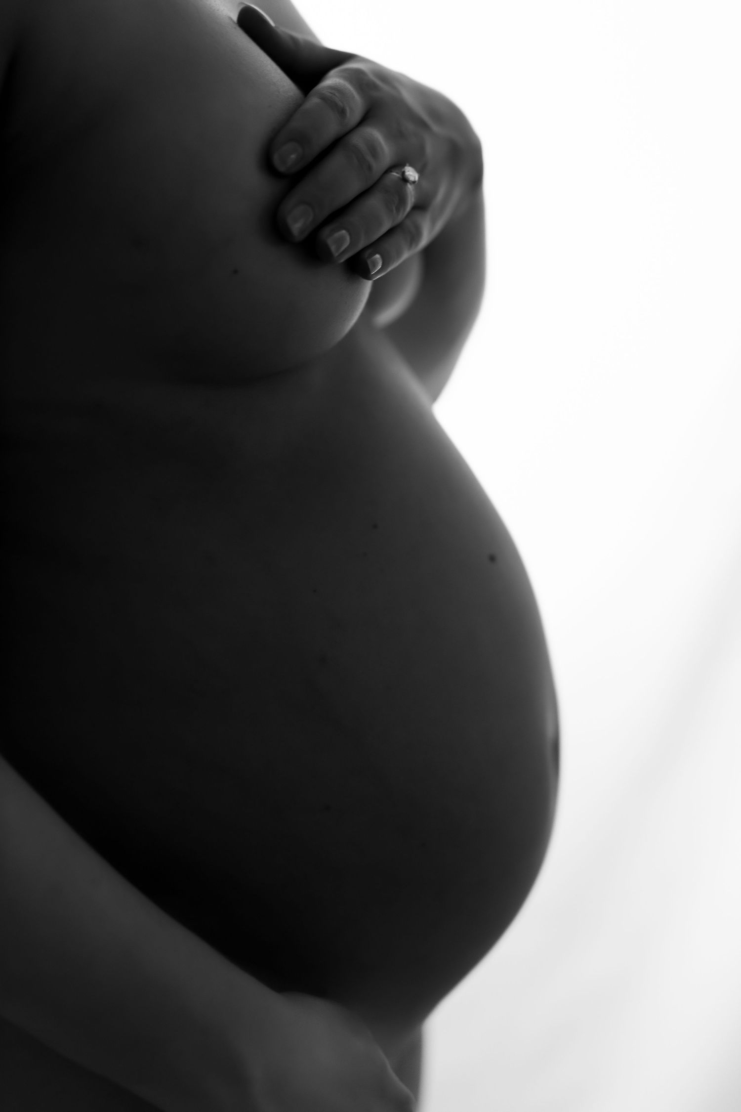Black and white artistic maternity photo showing a pregnant belly silhouette with gentle hand placement.