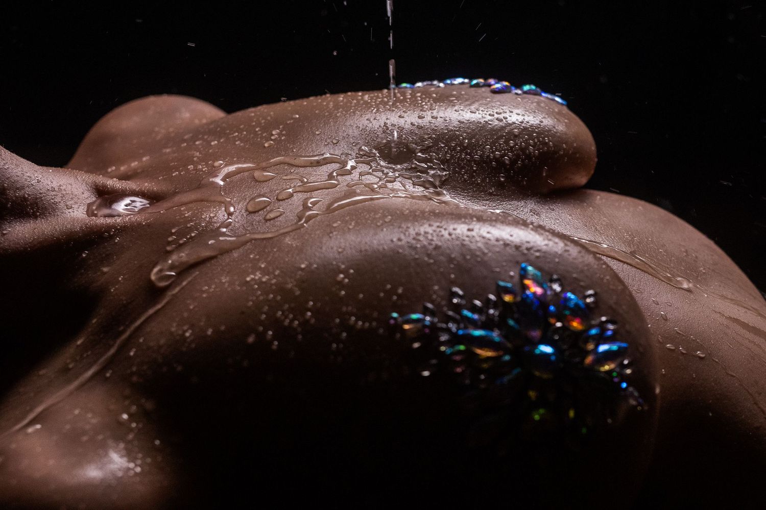 Artistic nude body covered in chocolate with sparkly blue glitter decoration and water droplets in dark lighting.