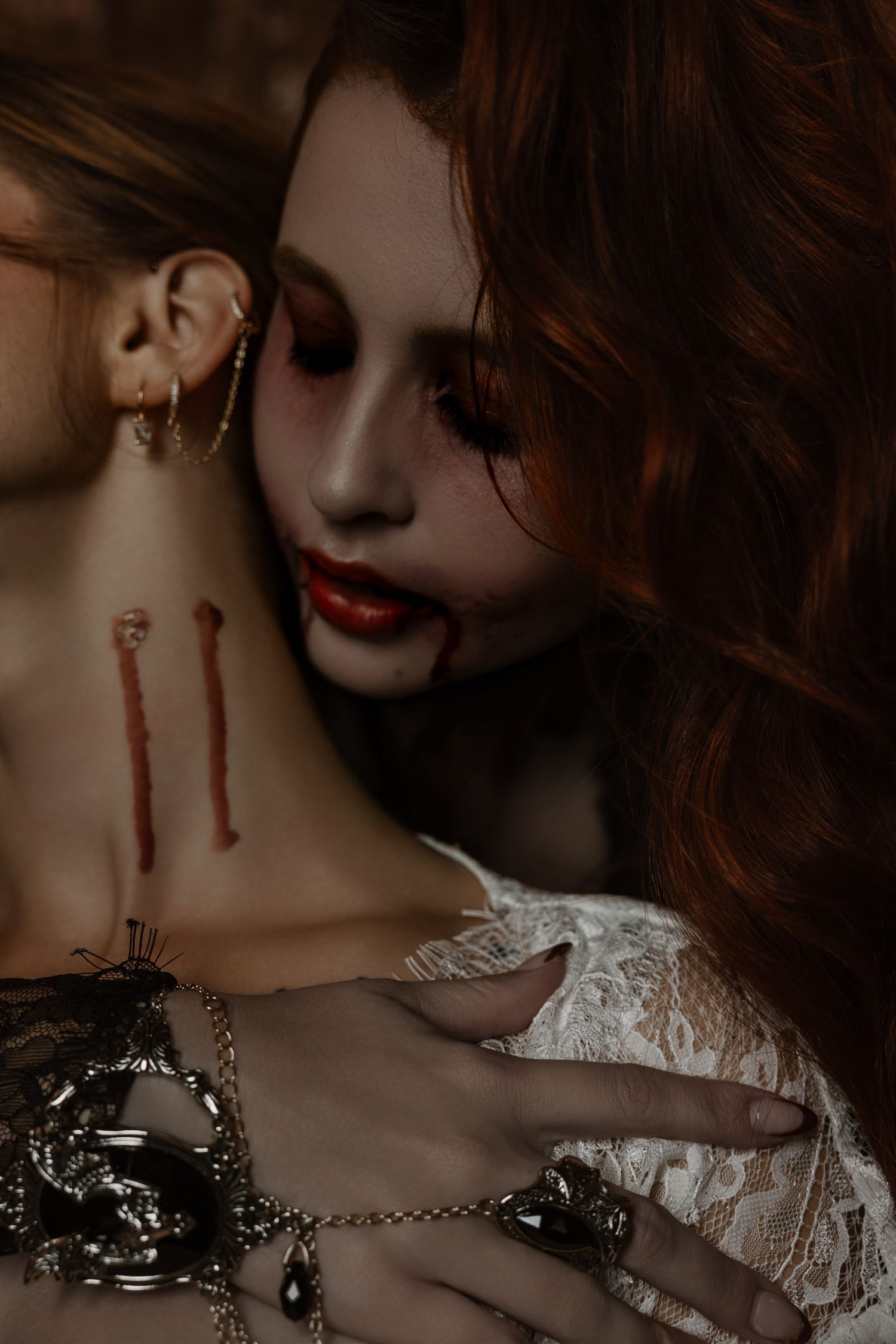 Gothic vampire woman with red lips and blood marks embracing another person in dark dramatic fantasy makeup.