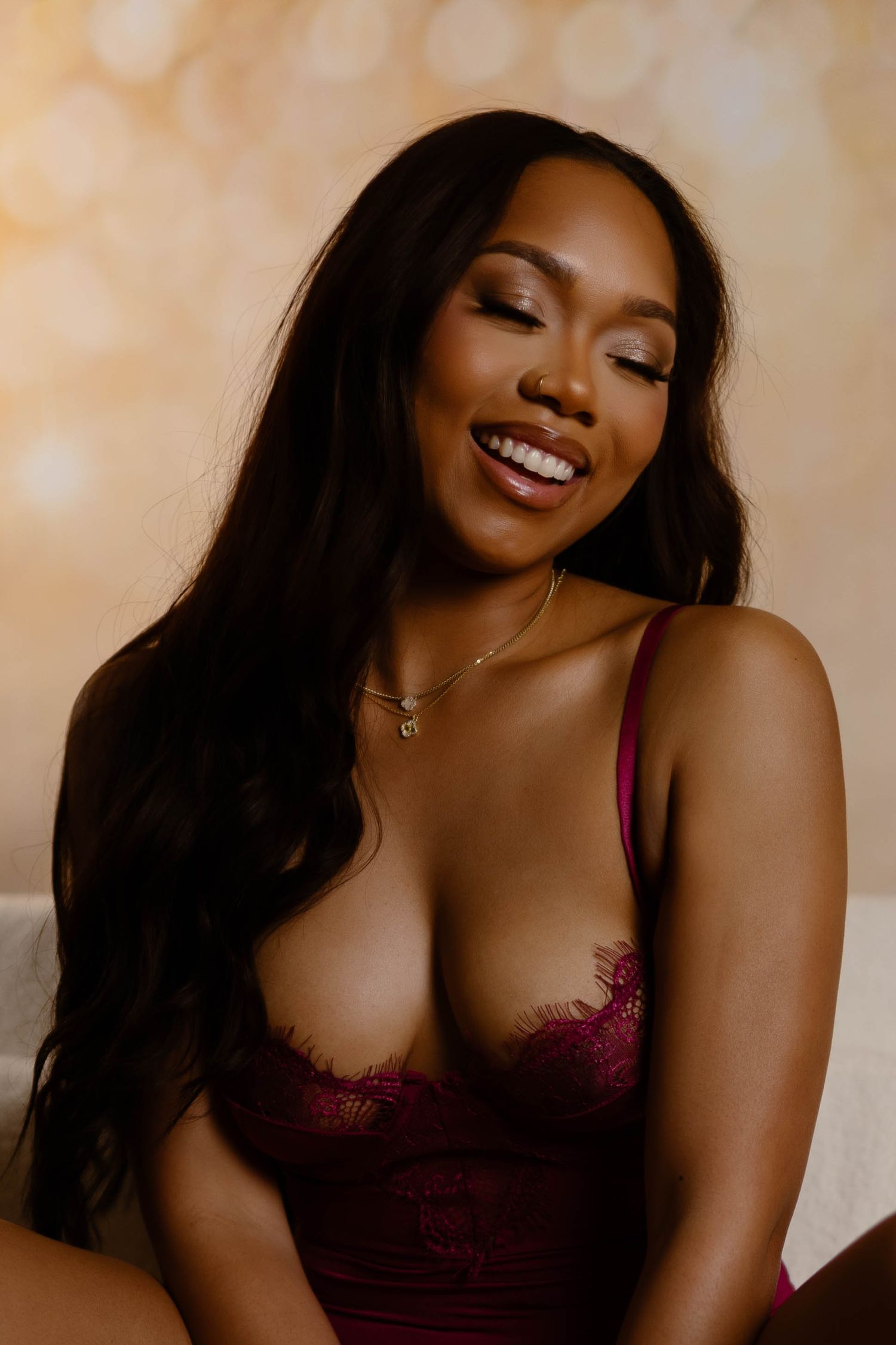 A person in burgundy lingerie smiles and poses against a beige background in a boudoir photo series.