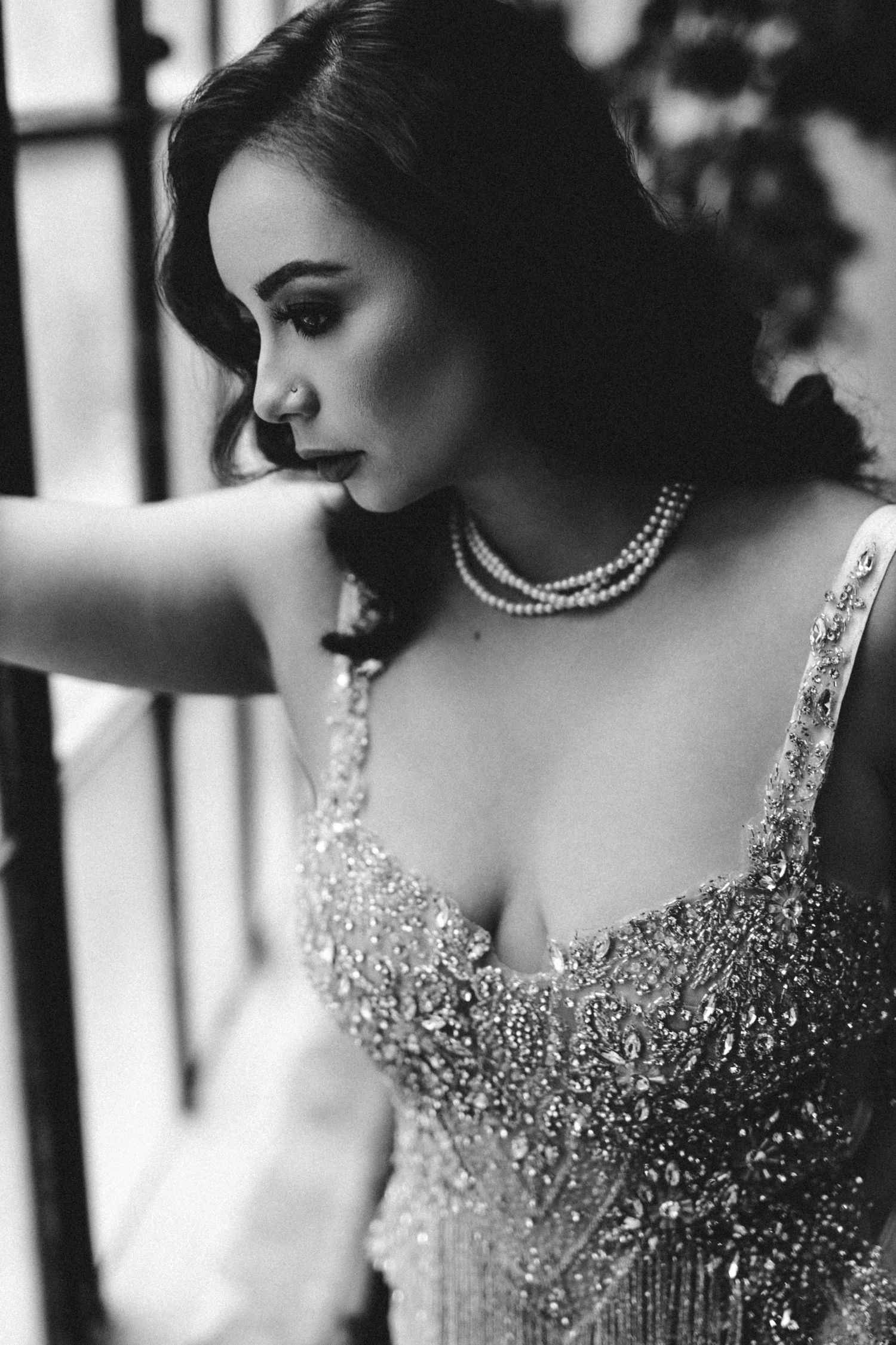 A black and white portrait showing an elegant figure in a beaded gown and pearl necklace with a classic vintage style.