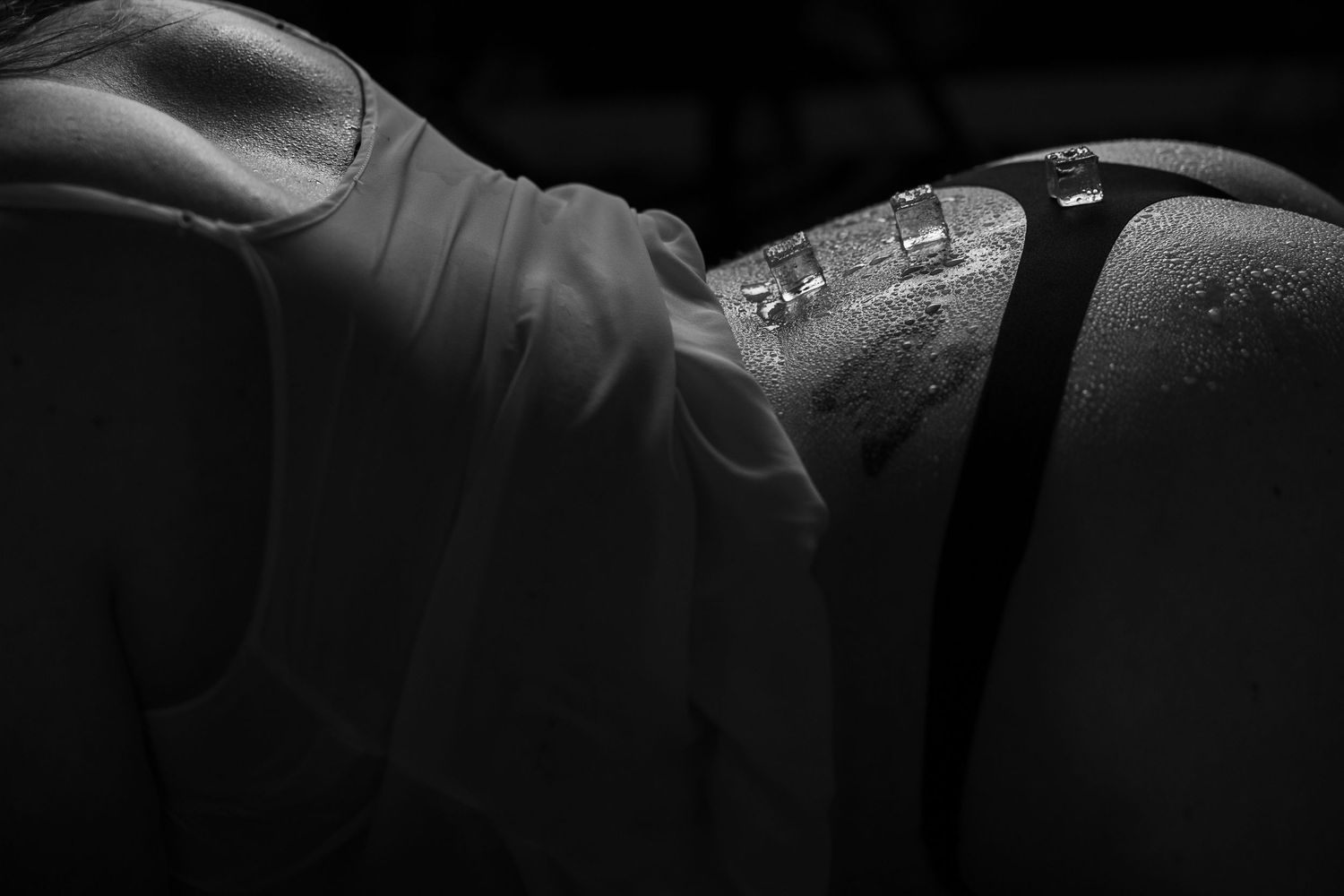 Silhouette bodyscape of woman's back with ice cubes against a dark background with dramatic lighting.