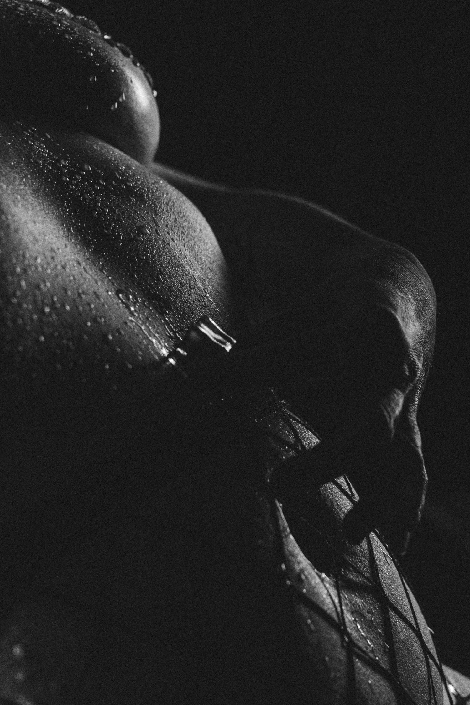 Artistic black and white close-up photograph showing water droplets on skin in dramatic lighting.