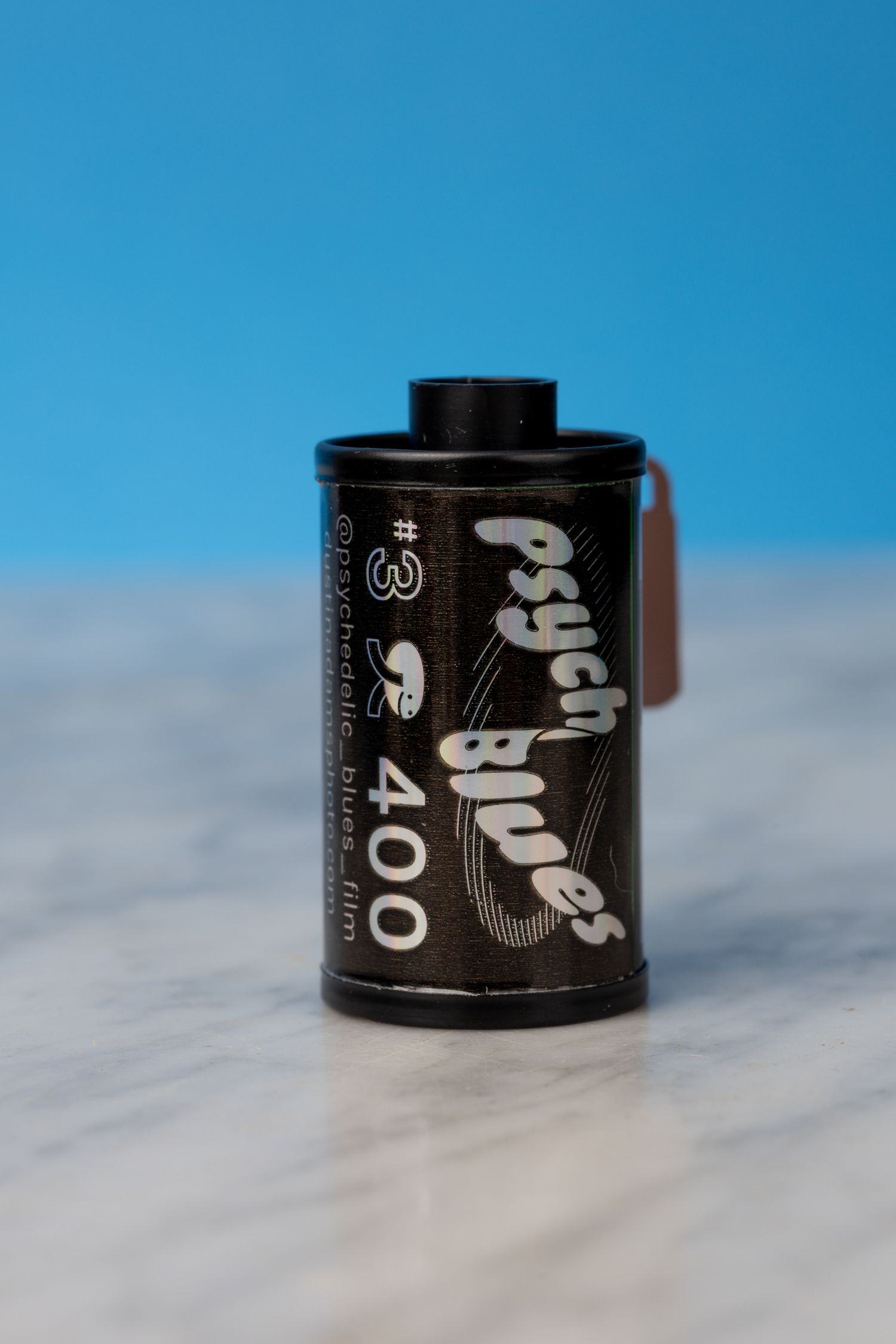A roll of Psysch Blues 400 film sitting on a marble surface with a blue background.