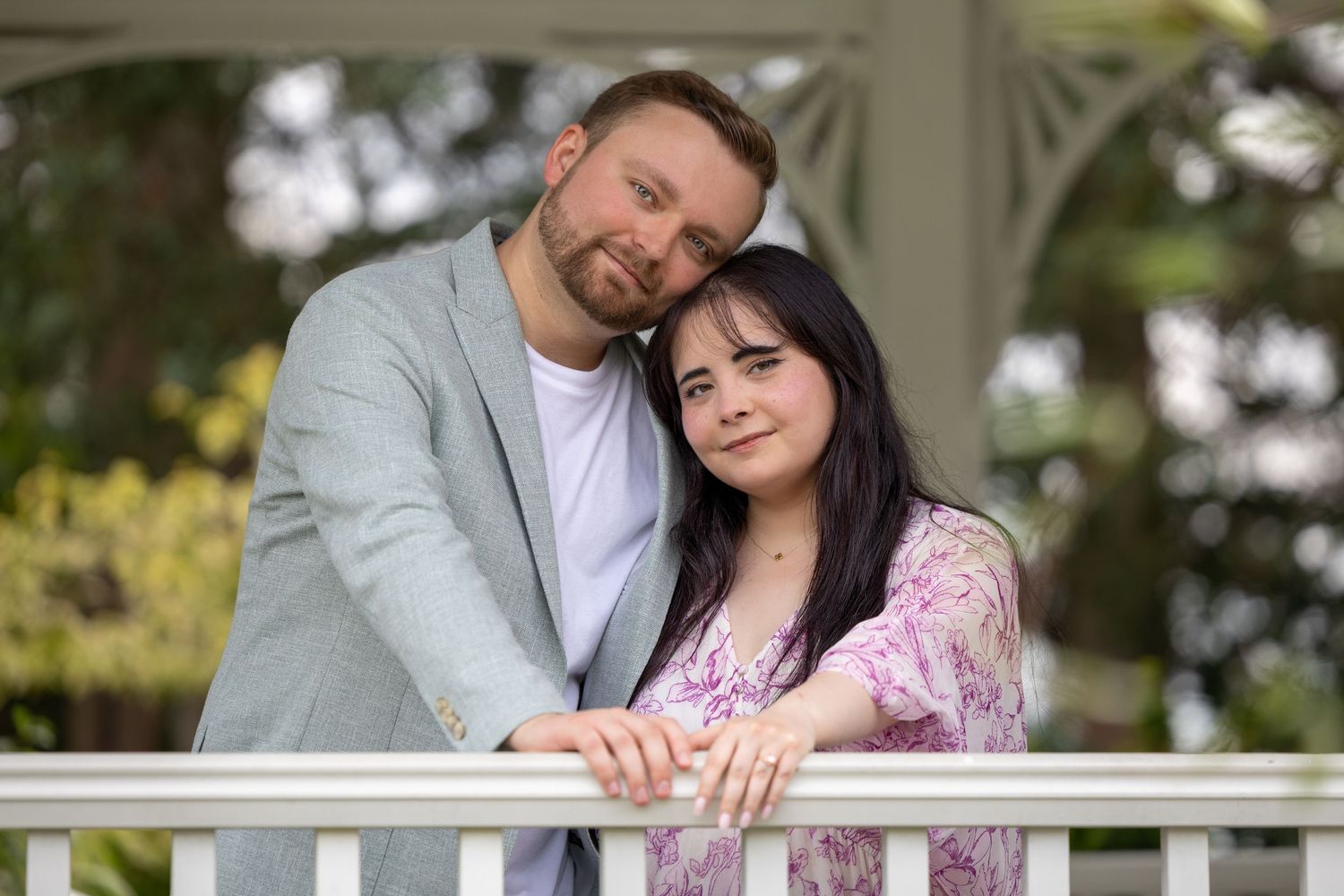 A couple stands in a white gazebo while leaning their heads together.