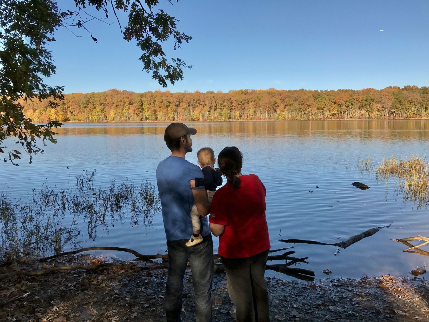 Two parents hold their toddler between them as they look out at the reflective surface of Burke Lake.
