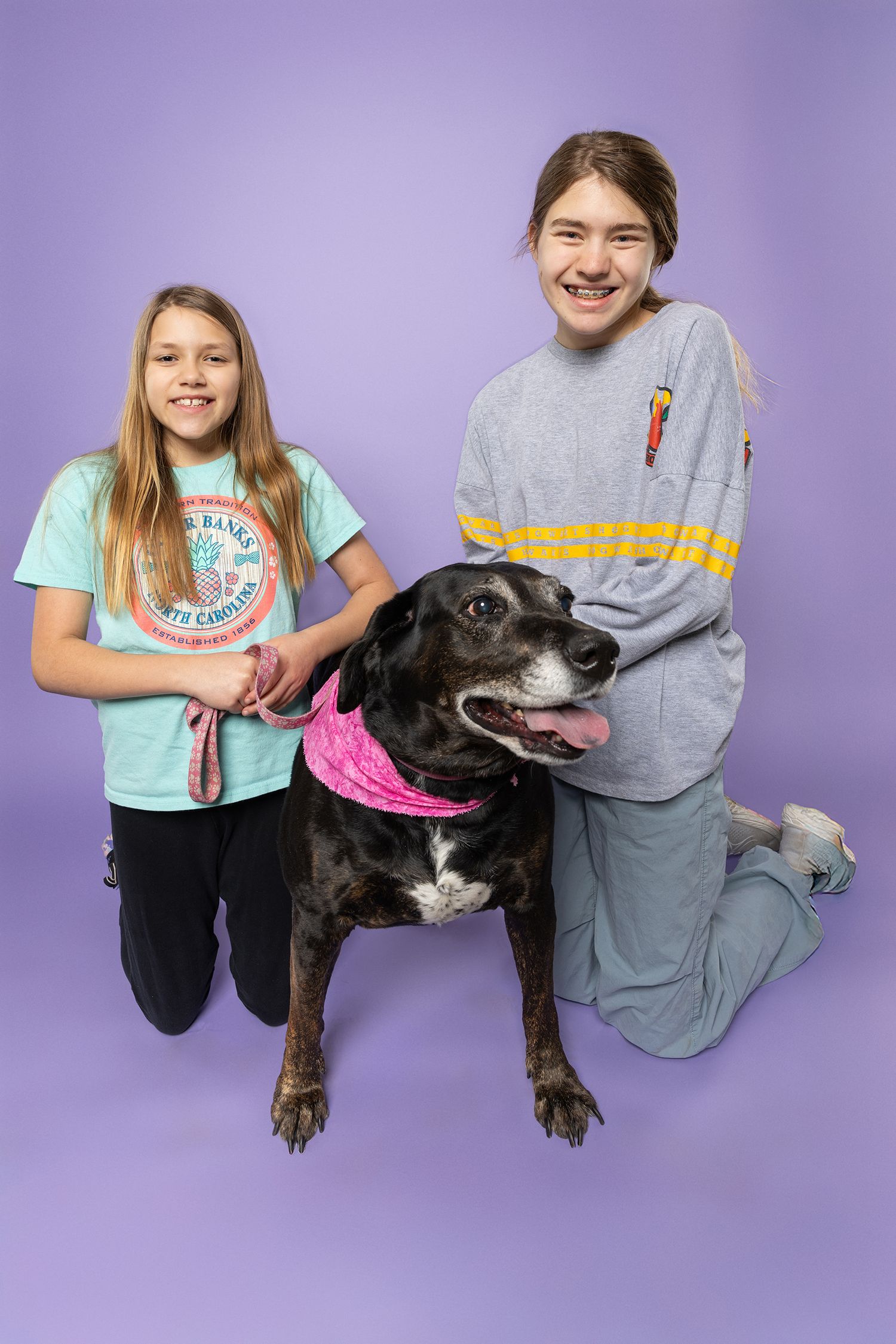 Two children pose for a portrait with their black lab