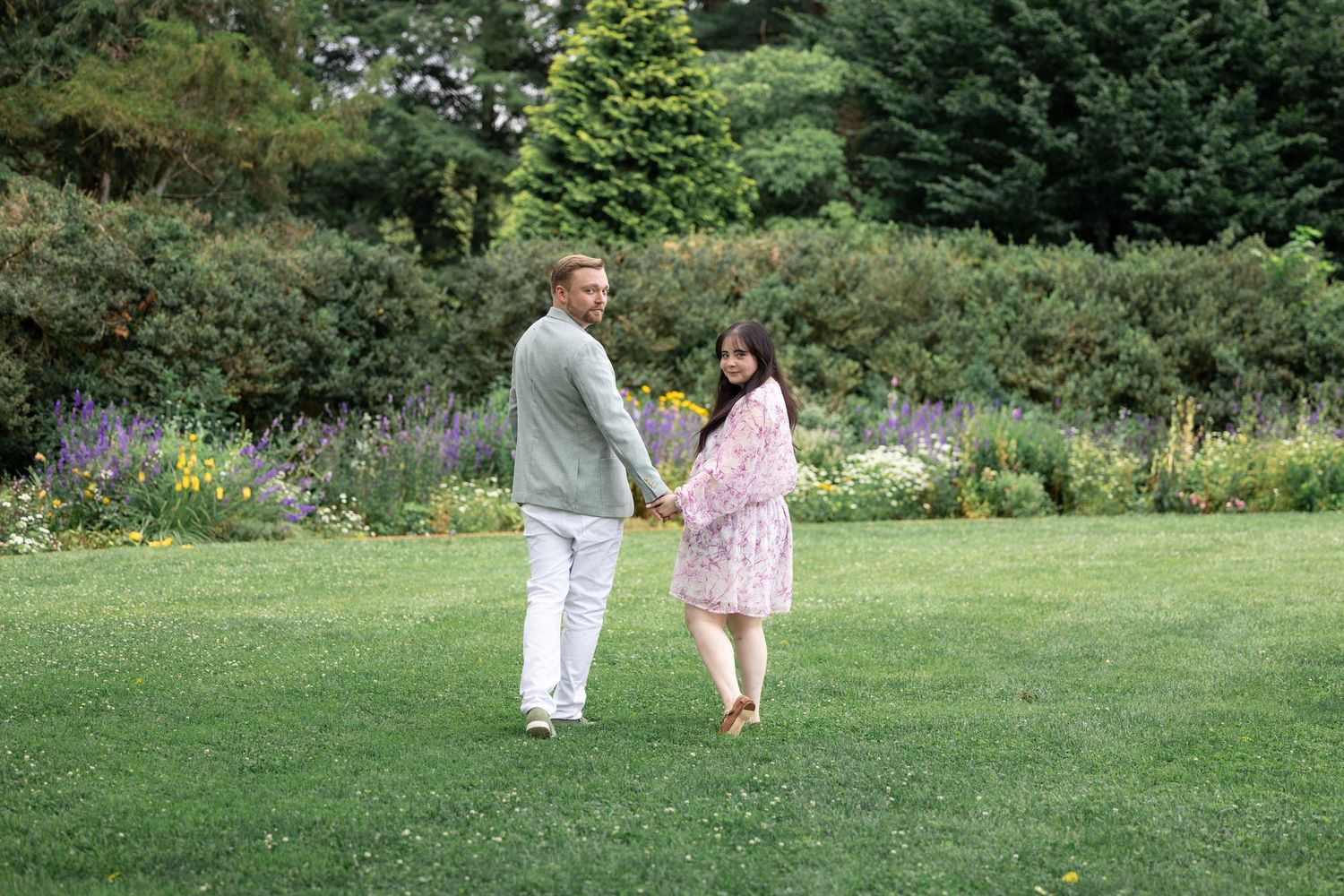 A couple walking though a green field, looks back at the camera.