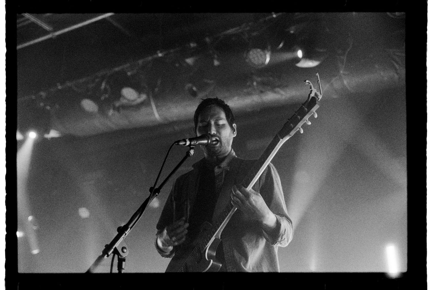 A black & white image on 35mm film of Teppei Teranishi of Thrice playing guitar on stage.