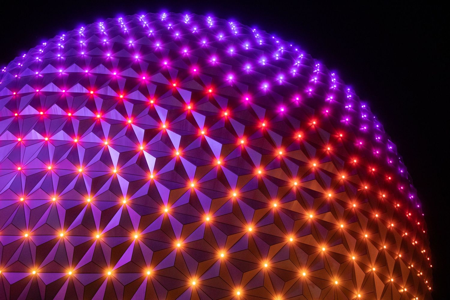 The geodesic sphere at Epcot at night, lit up in orange, pinks, and purples