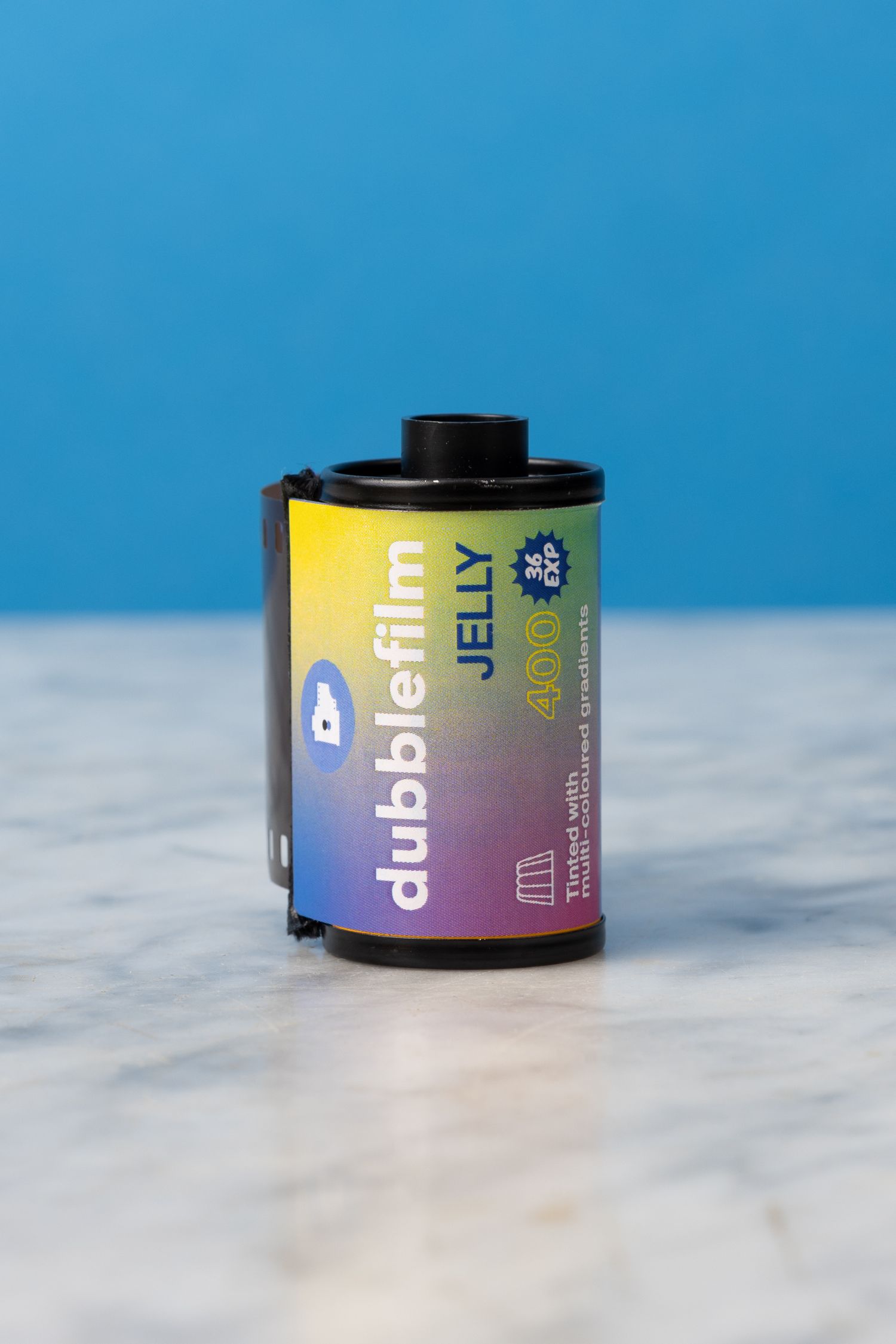 A roll of Dubblefim Jelly 400 film sitting on a marble surface with a blue background.