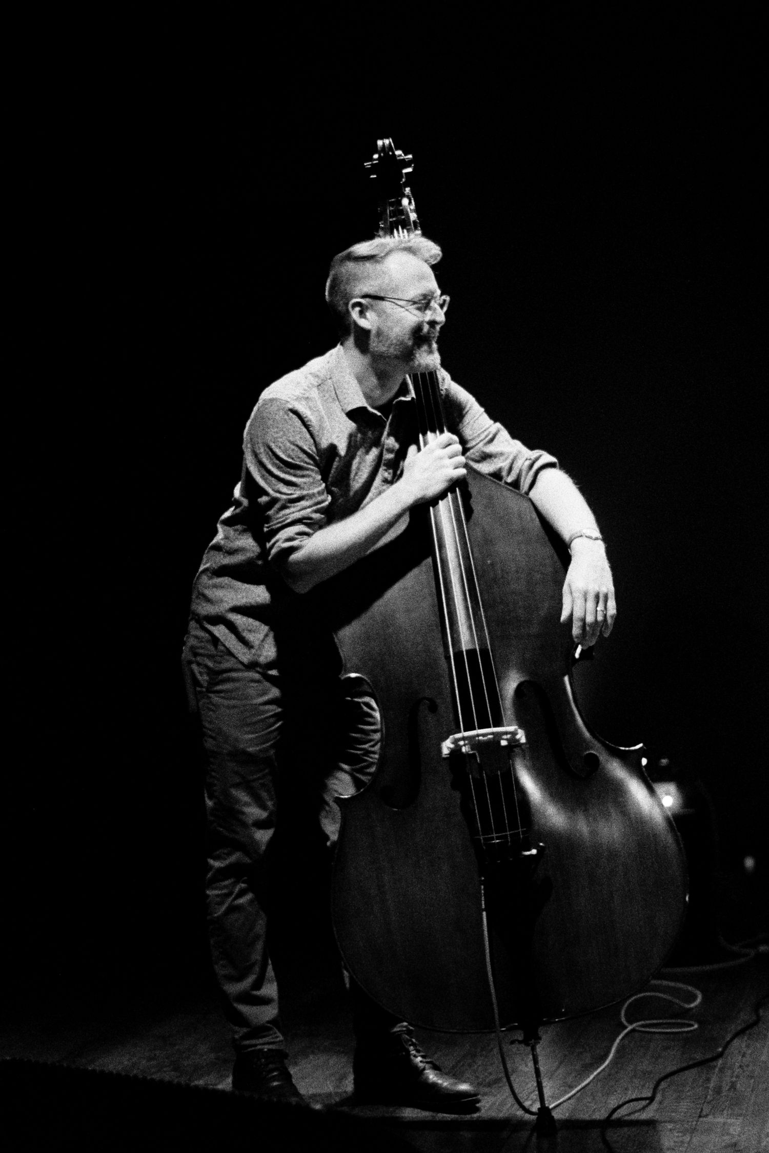 Black & white photo of a bassist relaxing on his upright bass.