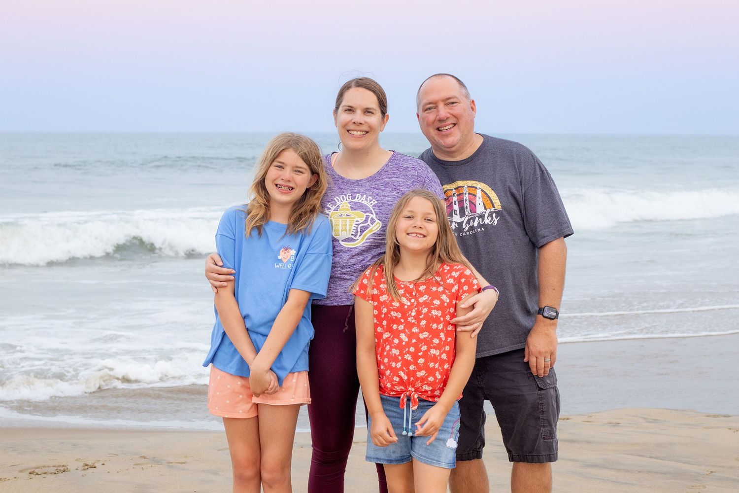 Portrait of a family of four on the beach with a pastel sky