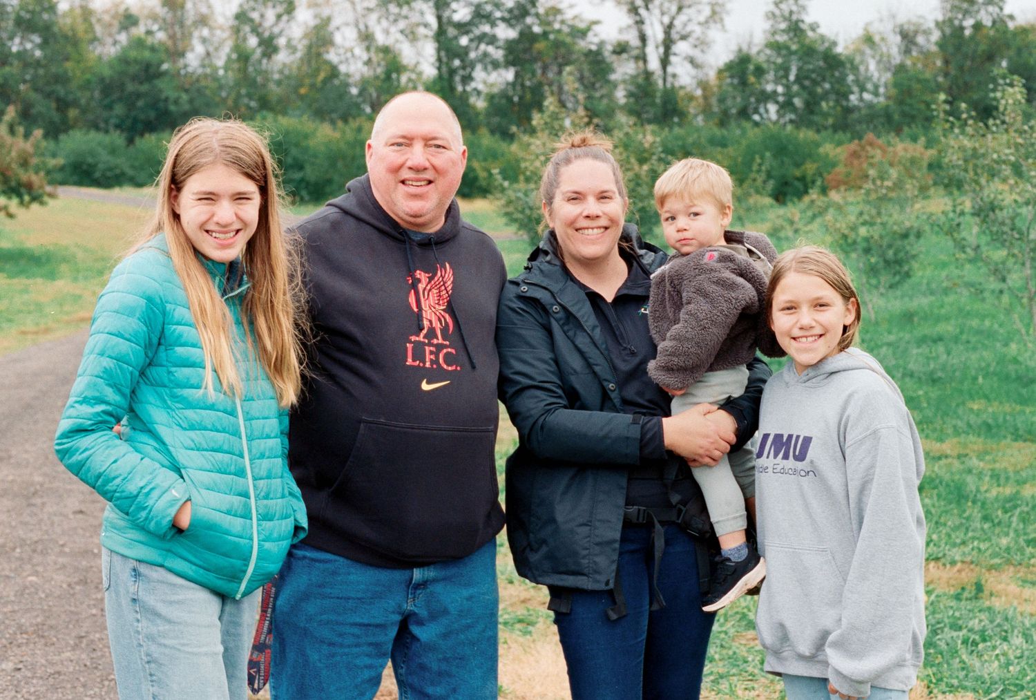 A medium-shot of a family of five standing in an apple orchard.