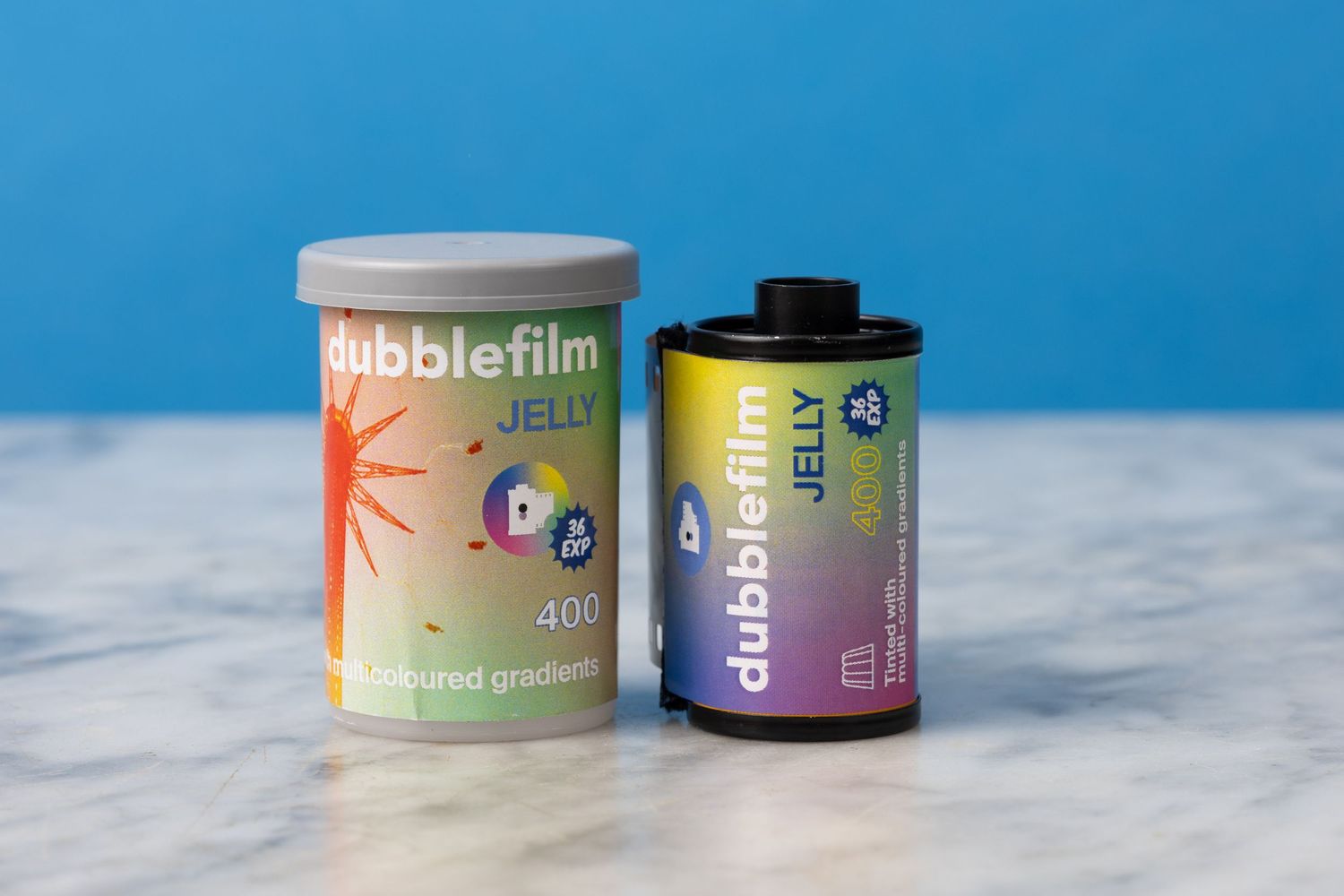 A roll of Dubblefim Jelly 400 film sitting on a marble surface with a blue background. The plastic film canister is next to it.