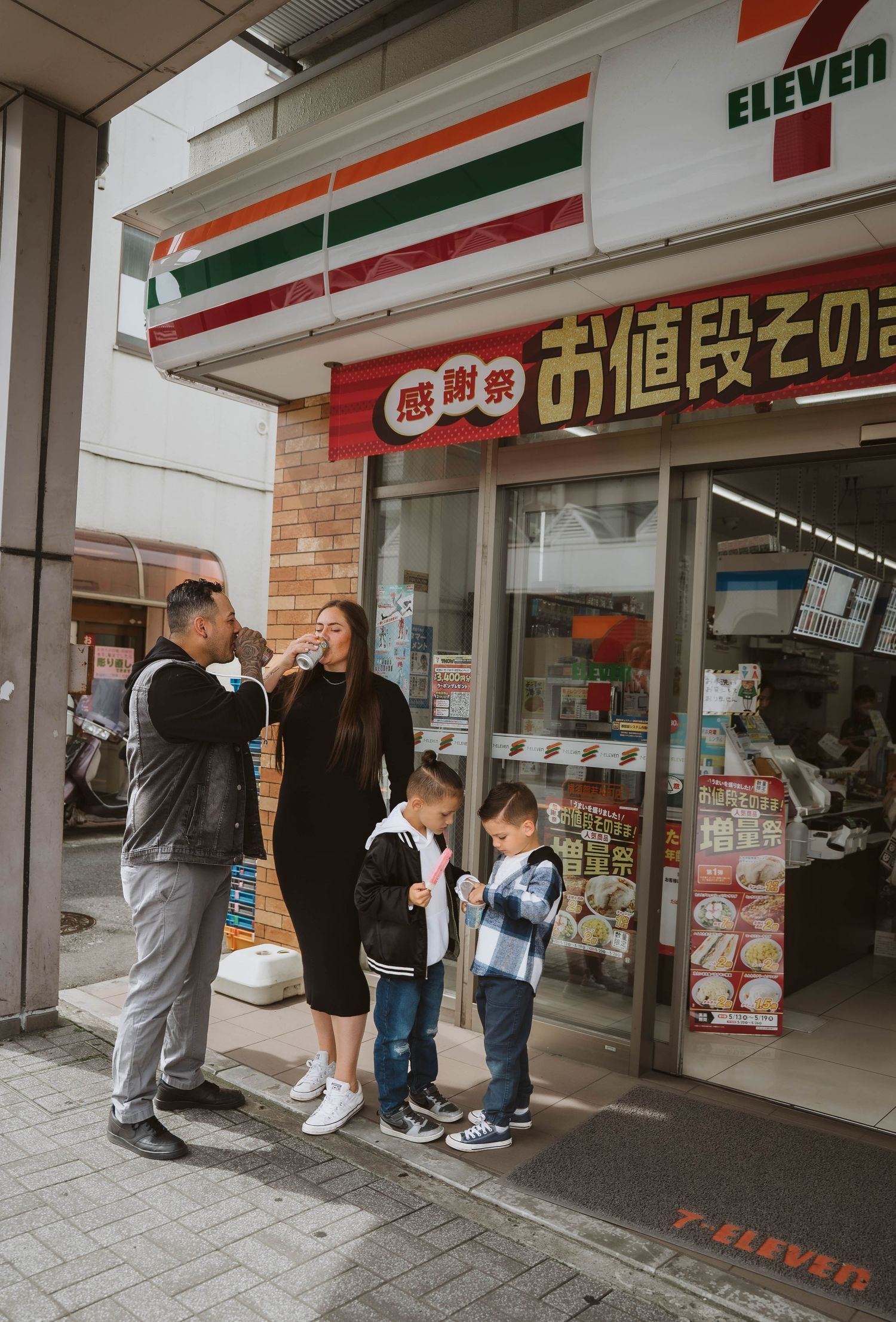 A group stands outside a 7-Eleven convenience store in Japan with Japanese signage visible.