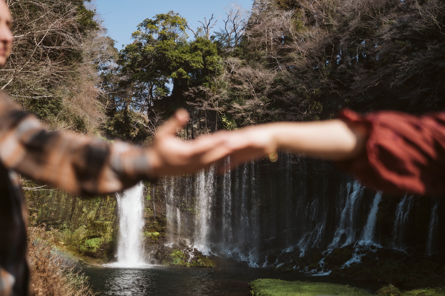 Scenic waterfall cascades down rocky cliffs surrounded by lush green forest in natural outdoor setting.