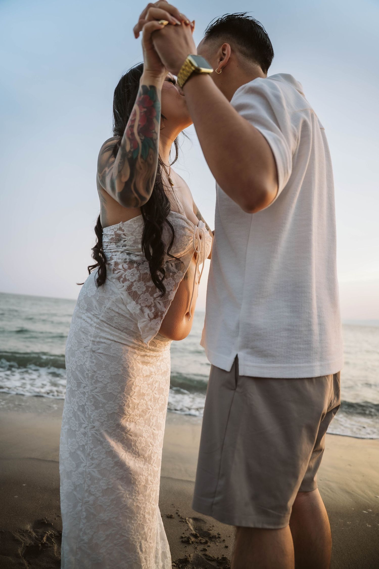 Couple embracing on beach during maternity photo session with ocean waves in background.
