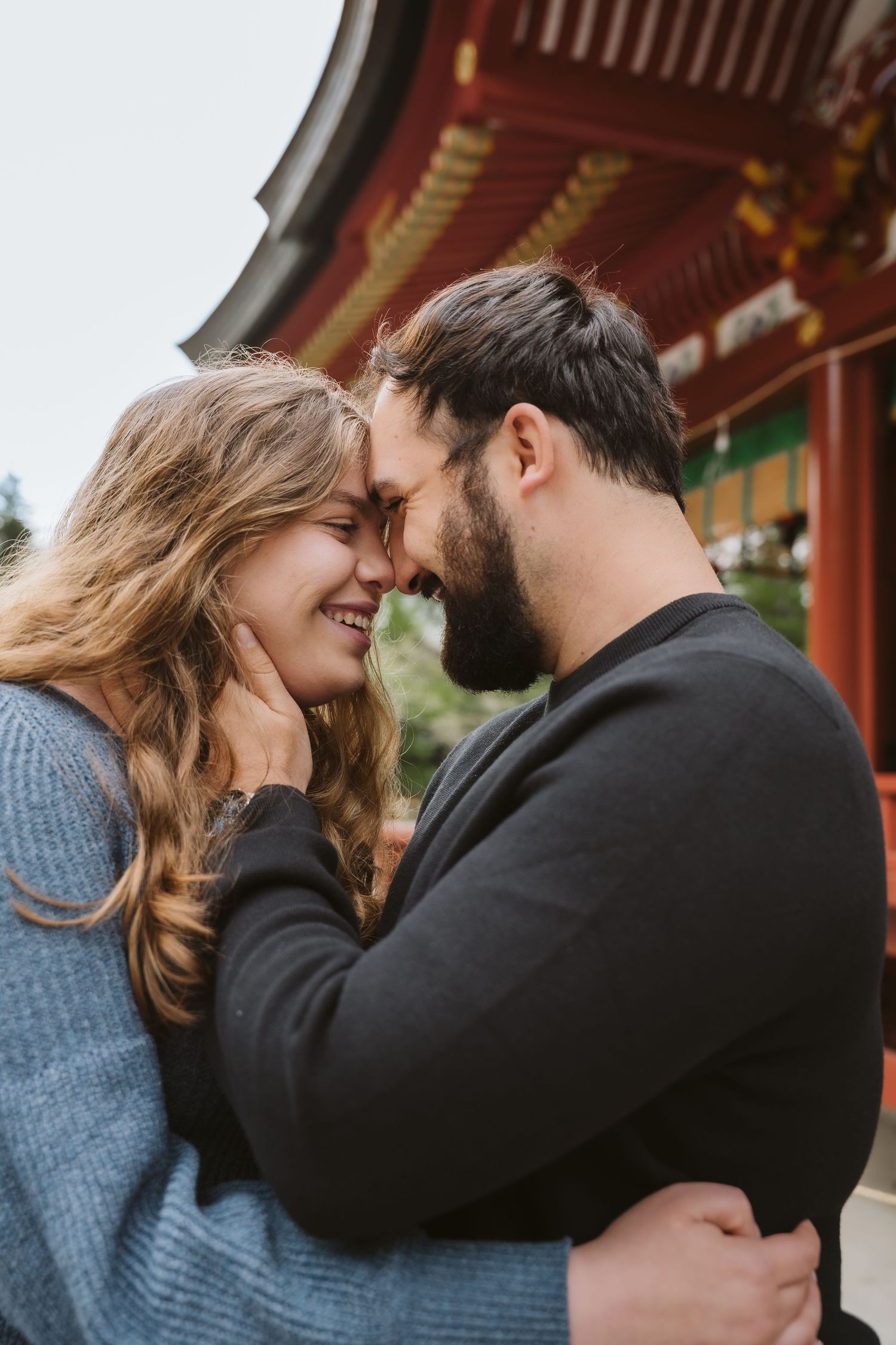 A romantic couple in warm sweaters share intimate moments while embracing at a traditional Asian temple.