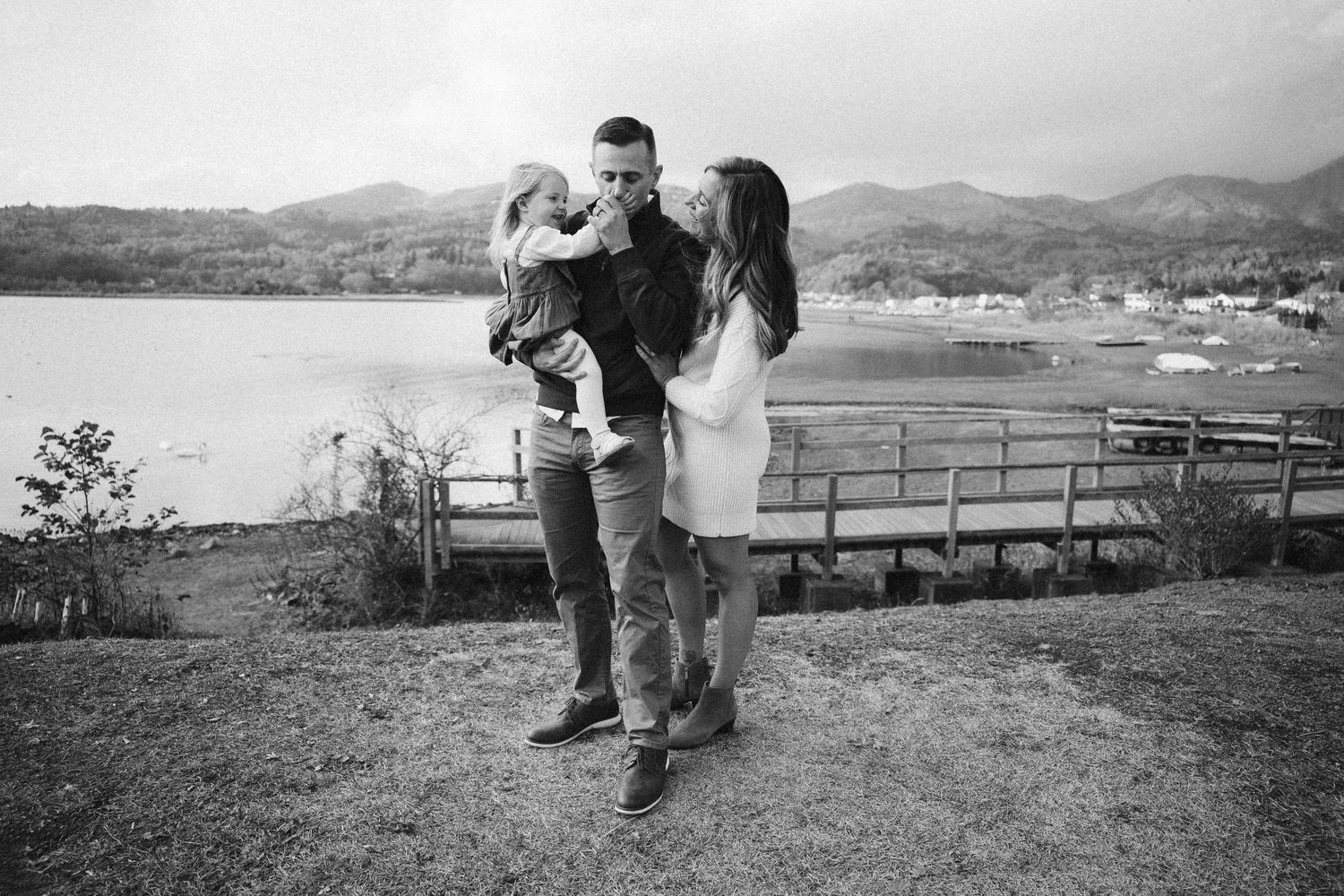 A romantic couple enjoys a scenic view from a hilltop overlooking a coastal landscape in black and white.