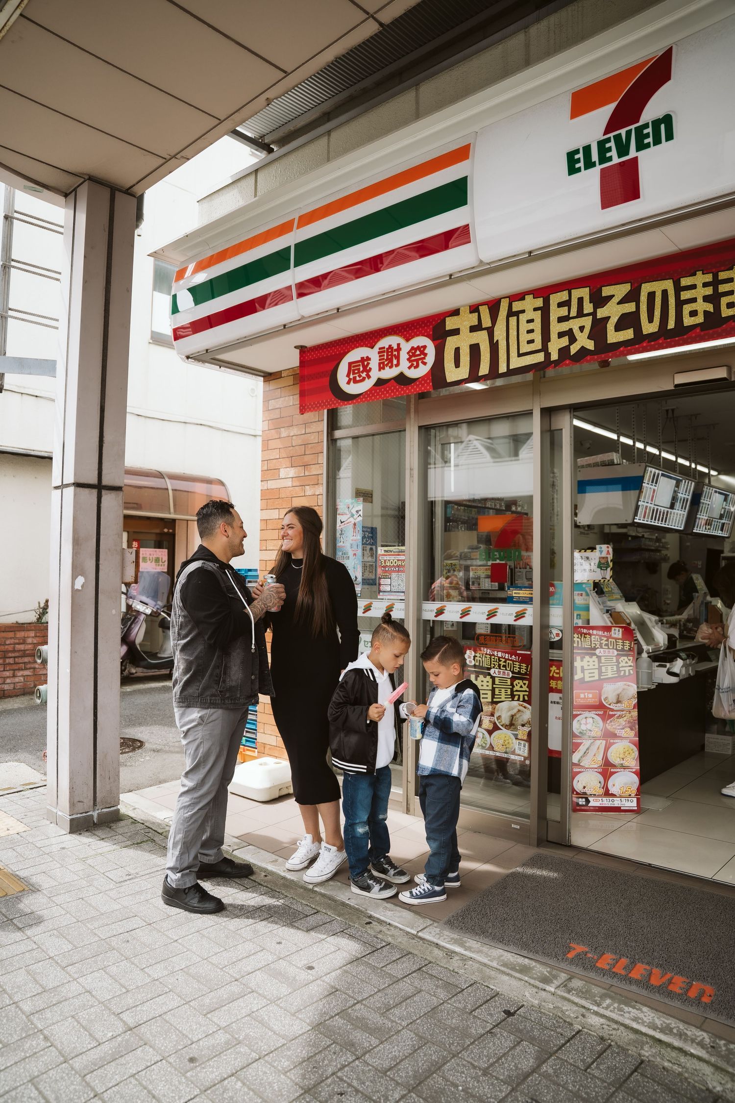 People waiting outside a 7-Eleven convenience store in Japan with signage visible in Japanese characters.