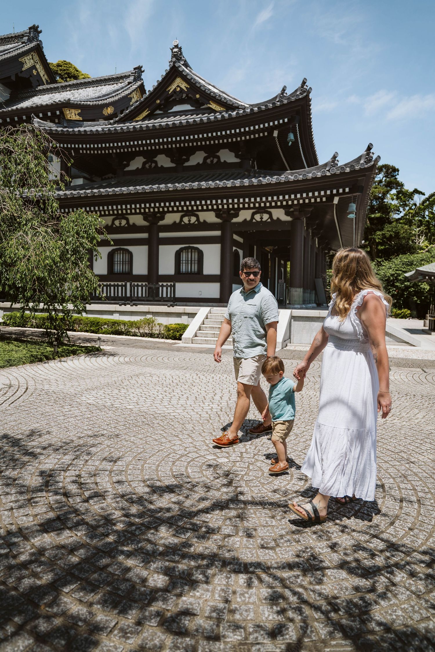 Family walking together near traditional Japanese temple architecture under blue skies.