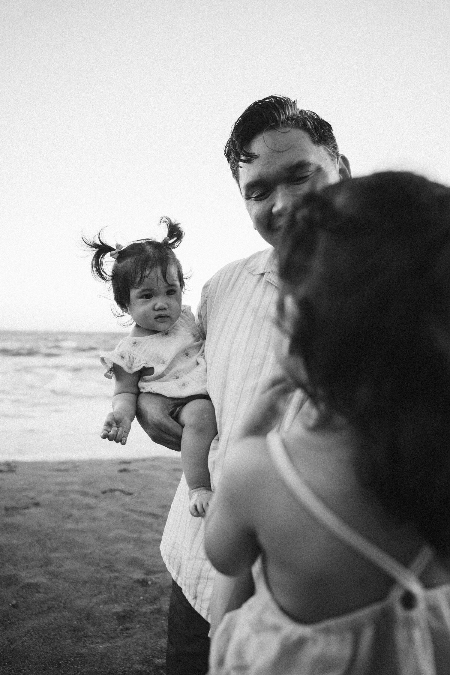 A candid black and white family moment captured on a sandy beach during a sunset photoshoot.