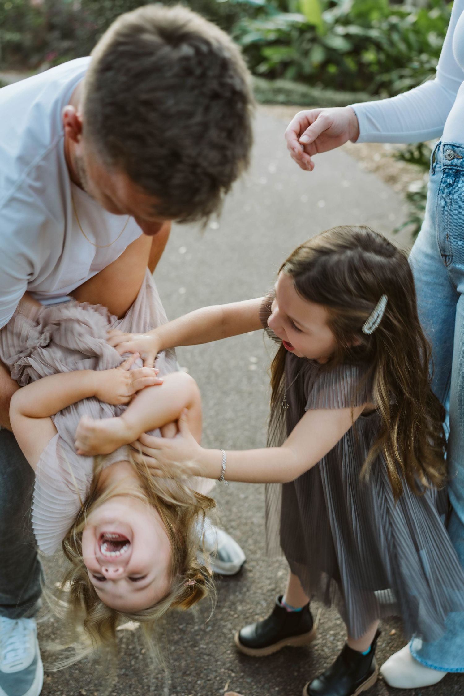 Children playing and laughing together outdoors with one child being playfully held upside down in a fun moment.