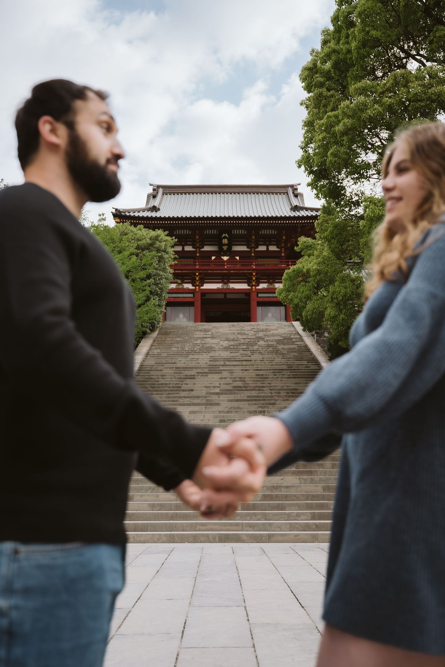 A couple holding hands walking up stone steps towards a traditional Japanese temple in a sequence of photos.