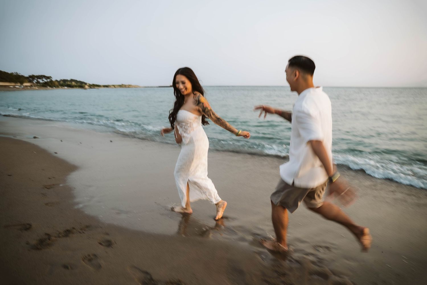 Romantic couple playing and splashing in the ocean waves at sunset along a scenic beach shoreline.