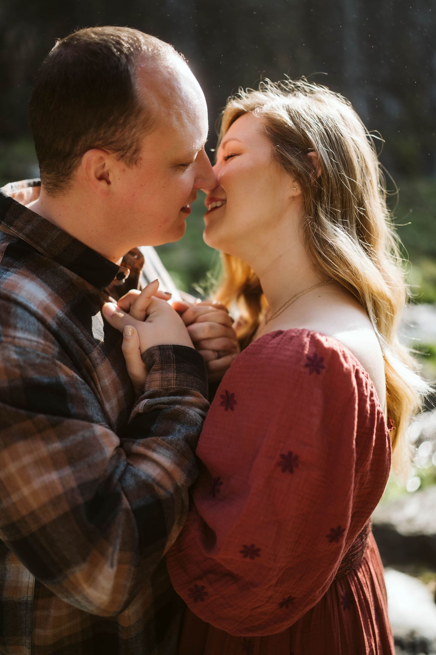 A couple in a plaid shirt and burgundy sweater share intimate moments in a sunlit outdoor setting.