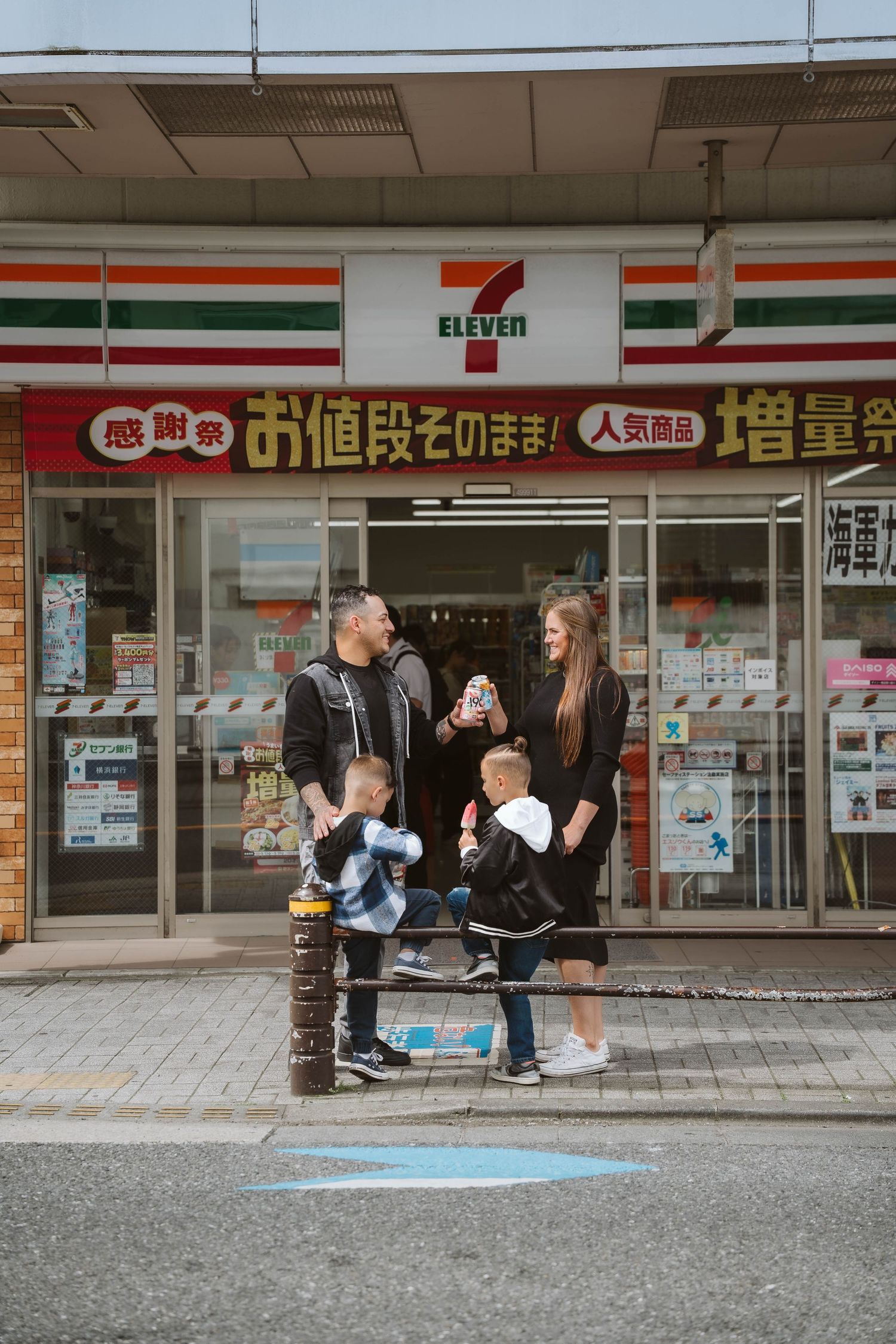 People resting outside a 7-Eleven convenience store in Japan with Japanese signage visible.