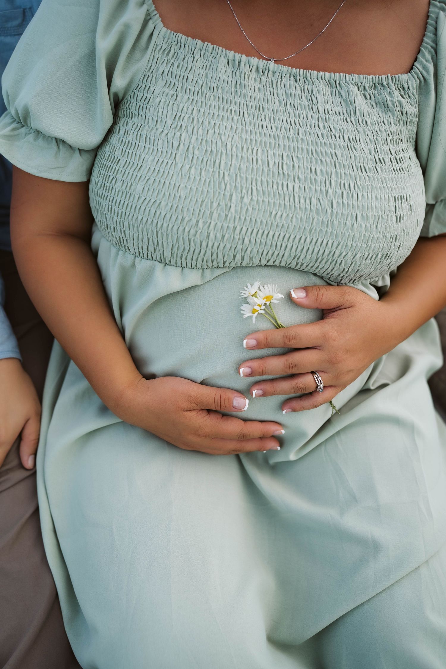 Close up of hands resting on a sage green smocked dress with a floral ring detail.