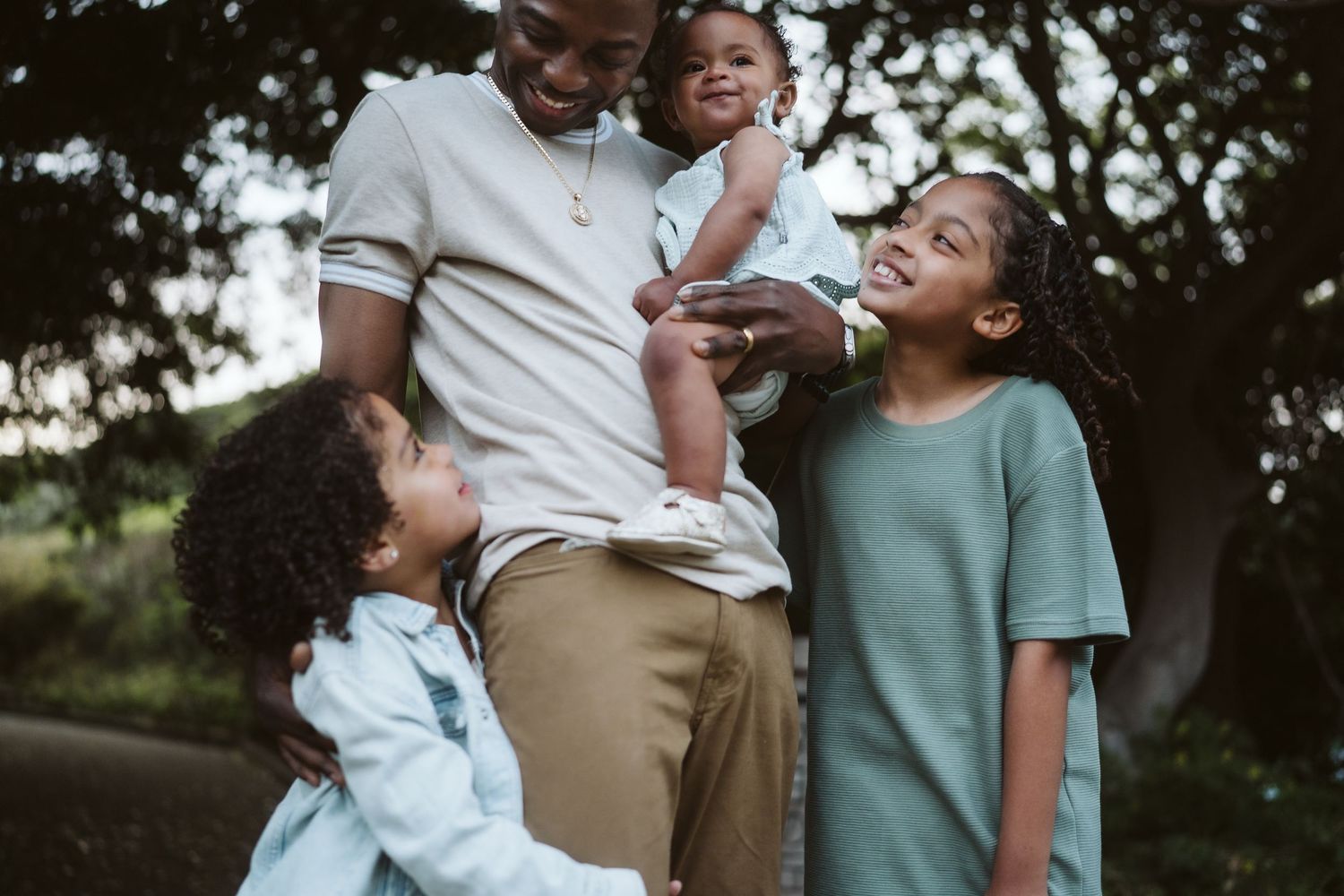 A family in casual clothing stands together outdoors in a park setting during golden hour lighting.