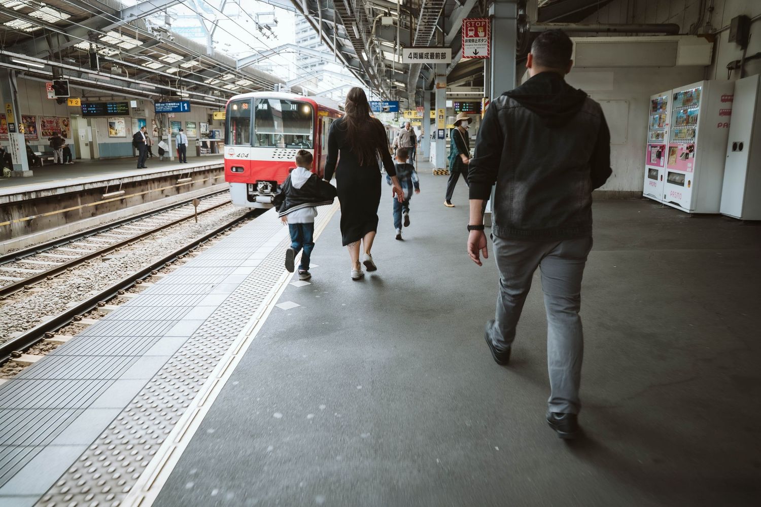 Passengers wait on a gray concrete subway platform with safety markings along the edge.