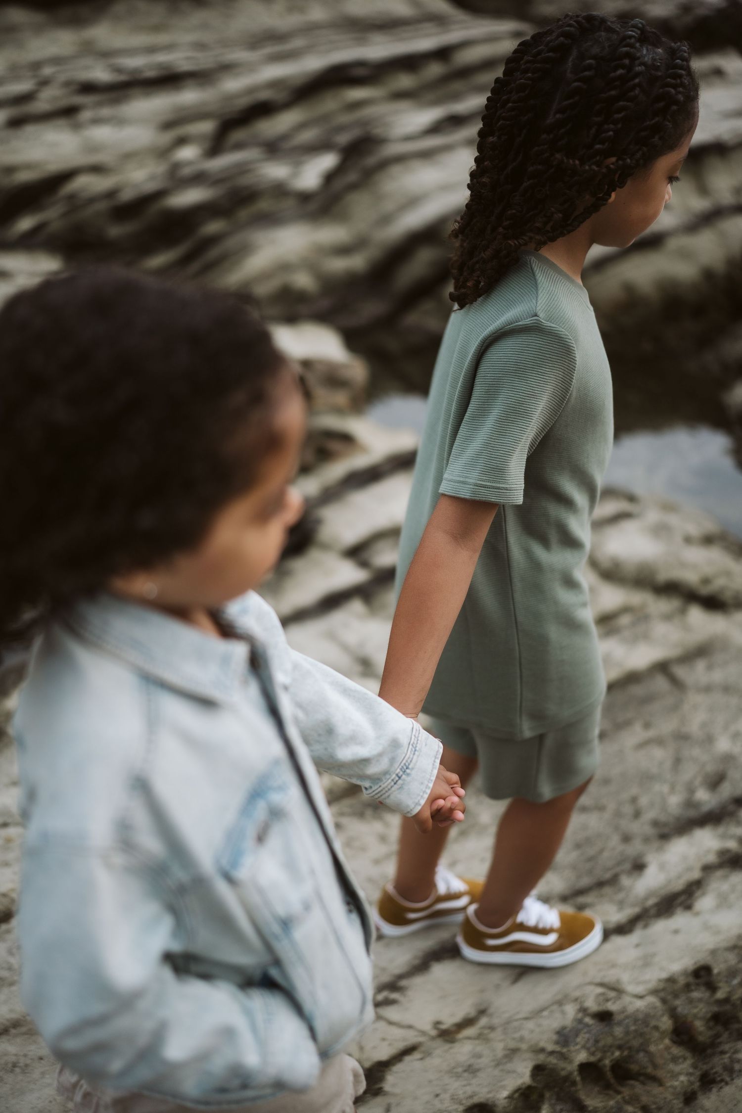 Close-up detail shot of people's feet and legs standing on rocky coastal terrain.