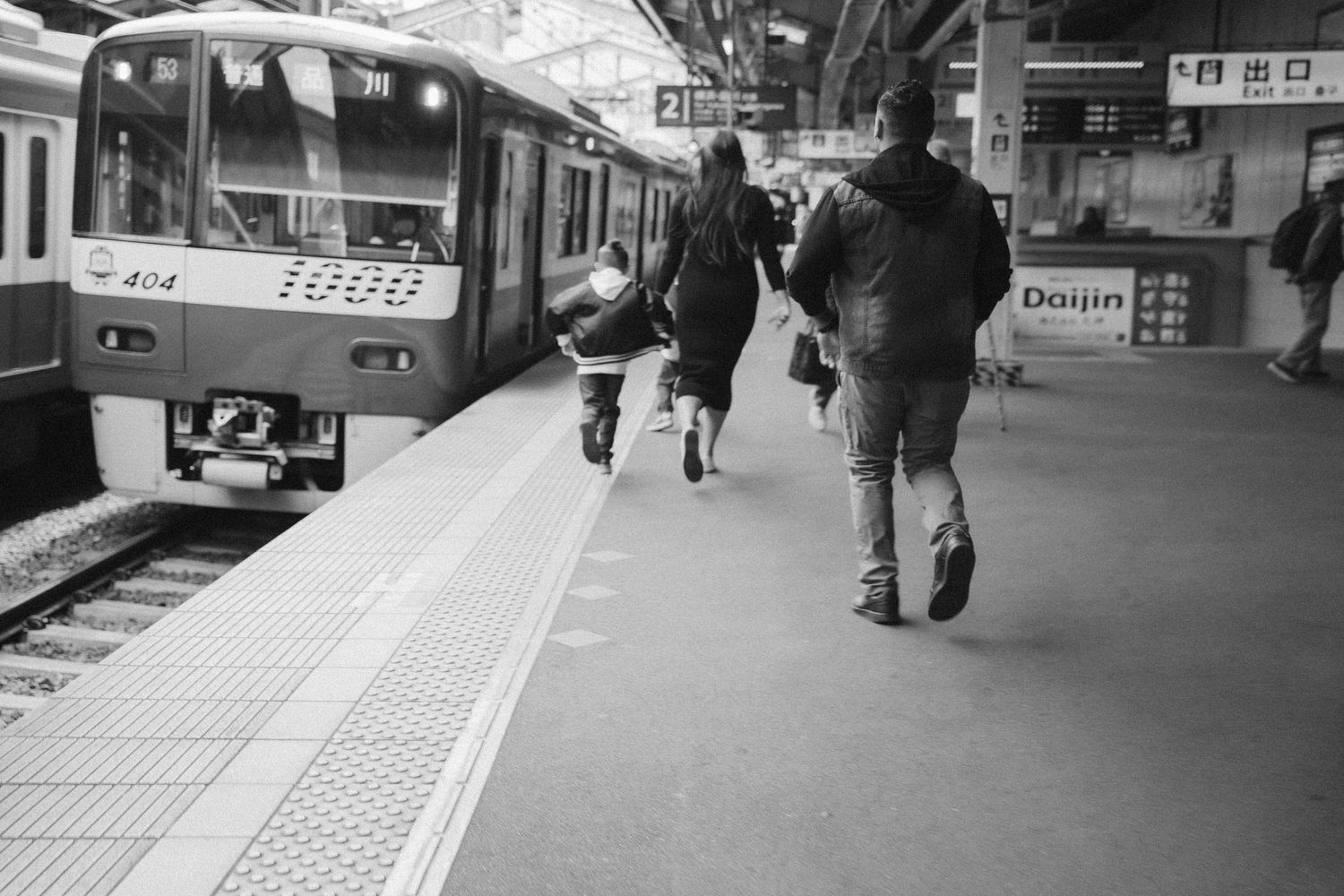 Black and white photograph of people walking along a train platform with tactile paving strips.