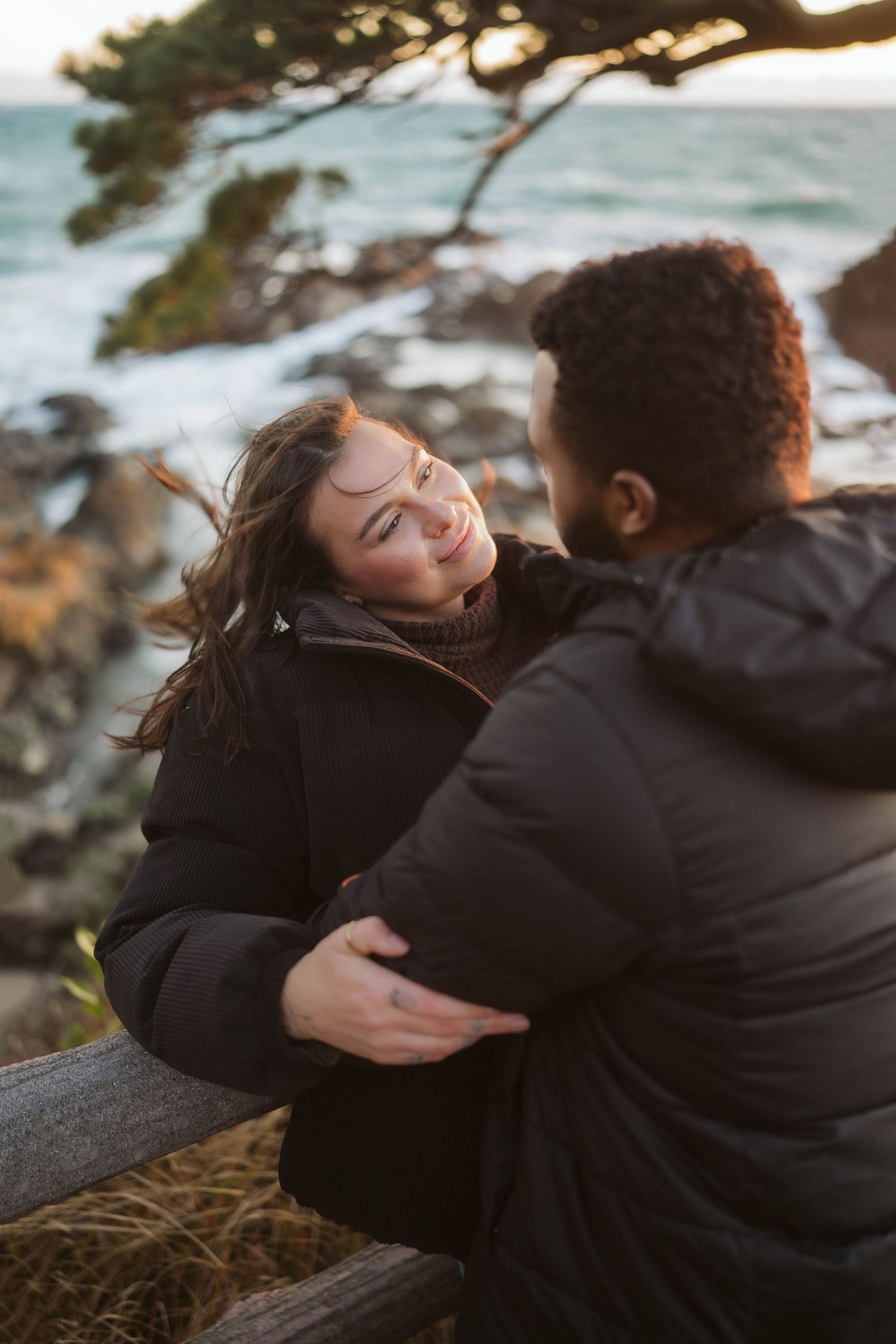 A tender moment shared between two people on a scenic coastal overlook at sunset.