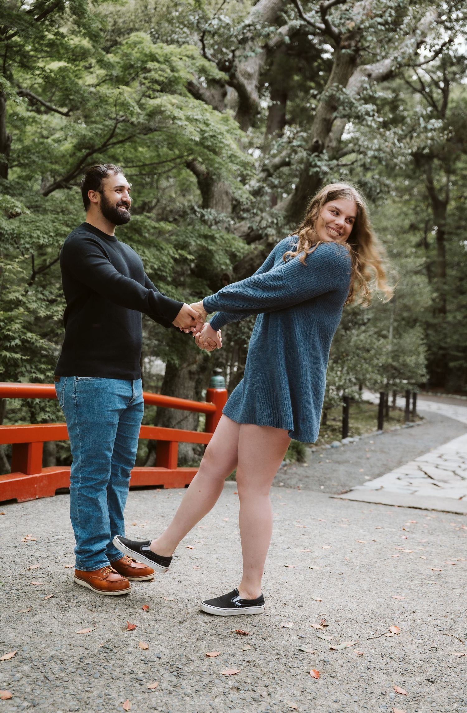 Couple dancing playfully together on gravel path with bright orange torii gates in background.