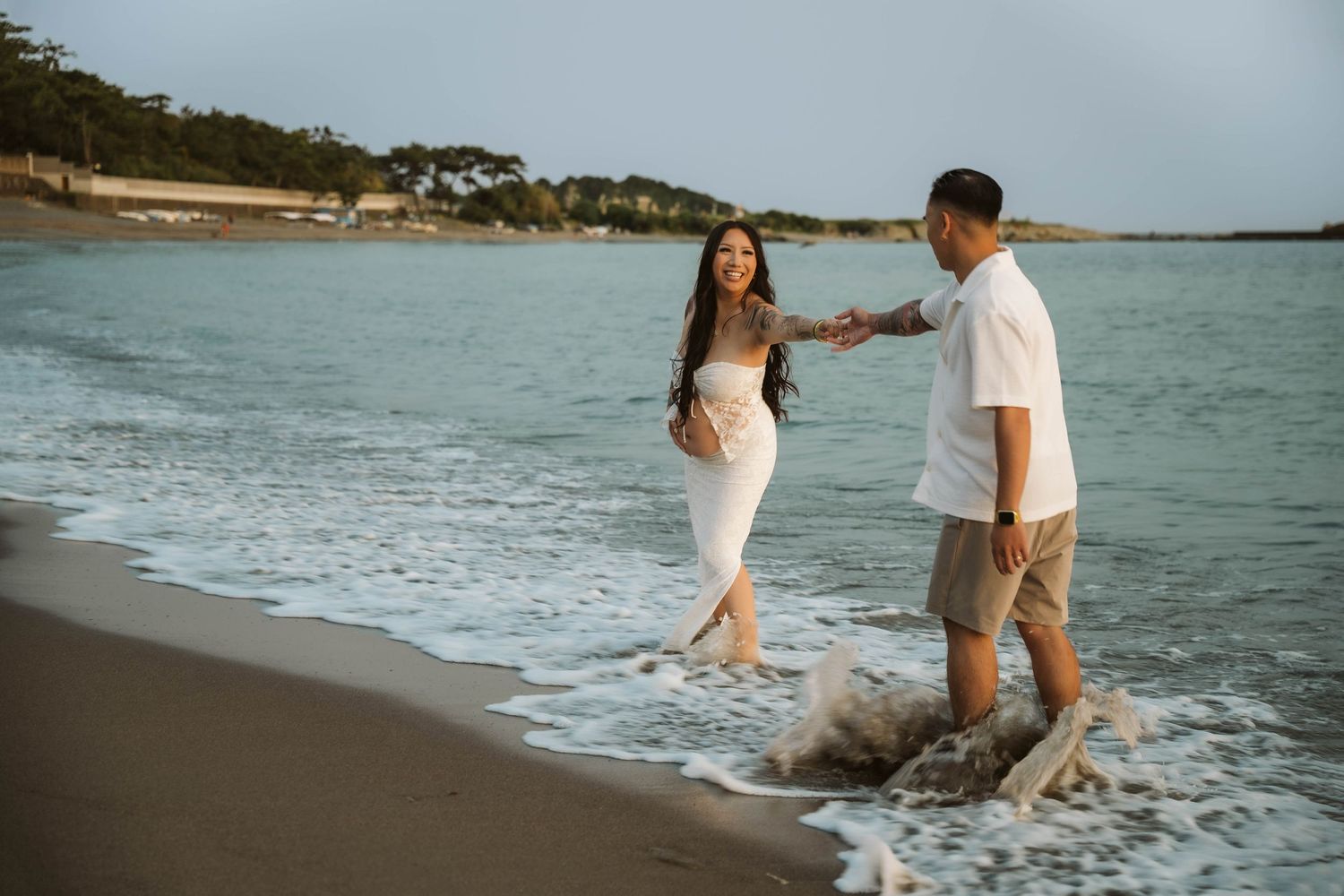 Couple walking and playing together along a scenic beach shoreline at sunset.