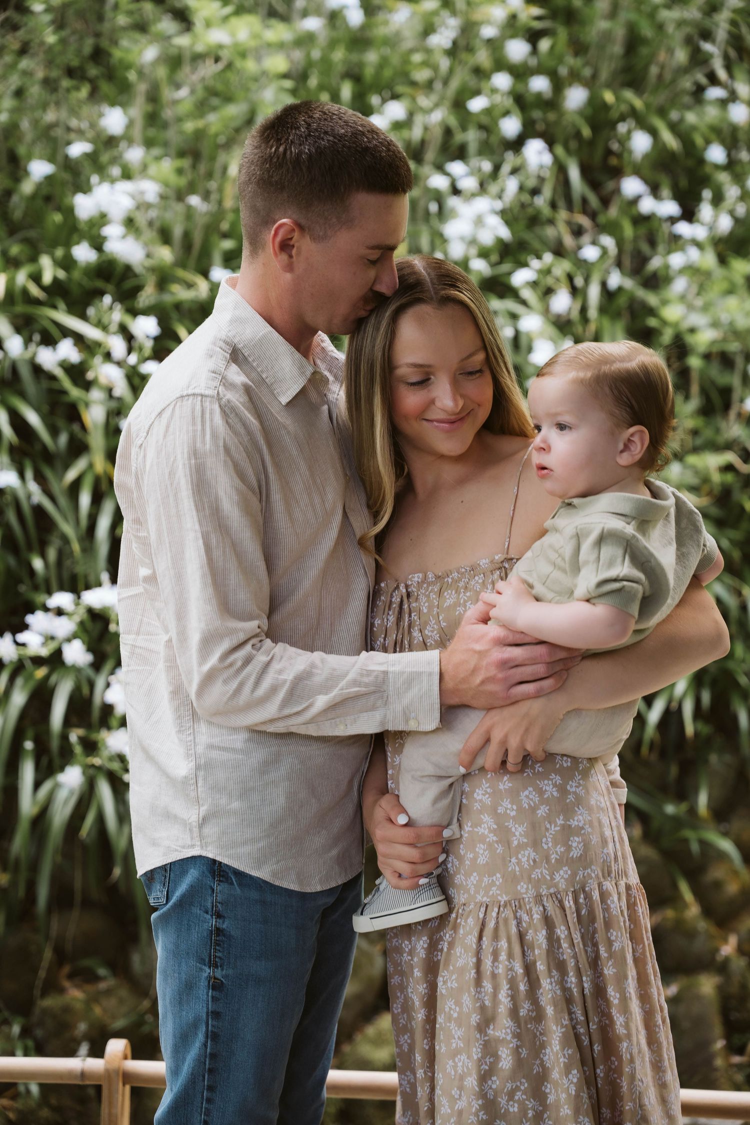 A family shares tender moments together in a garden setting wearing casual white and floral clothing.