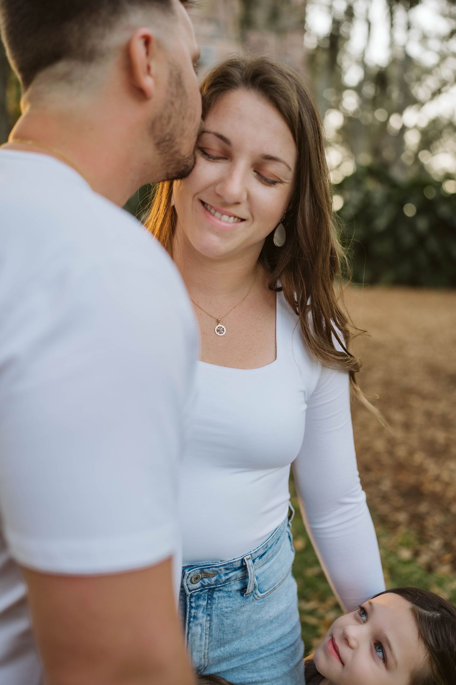 A loving couple shares a tender moment outdoors in soft natural lighting while wearing casual white tops and denim.